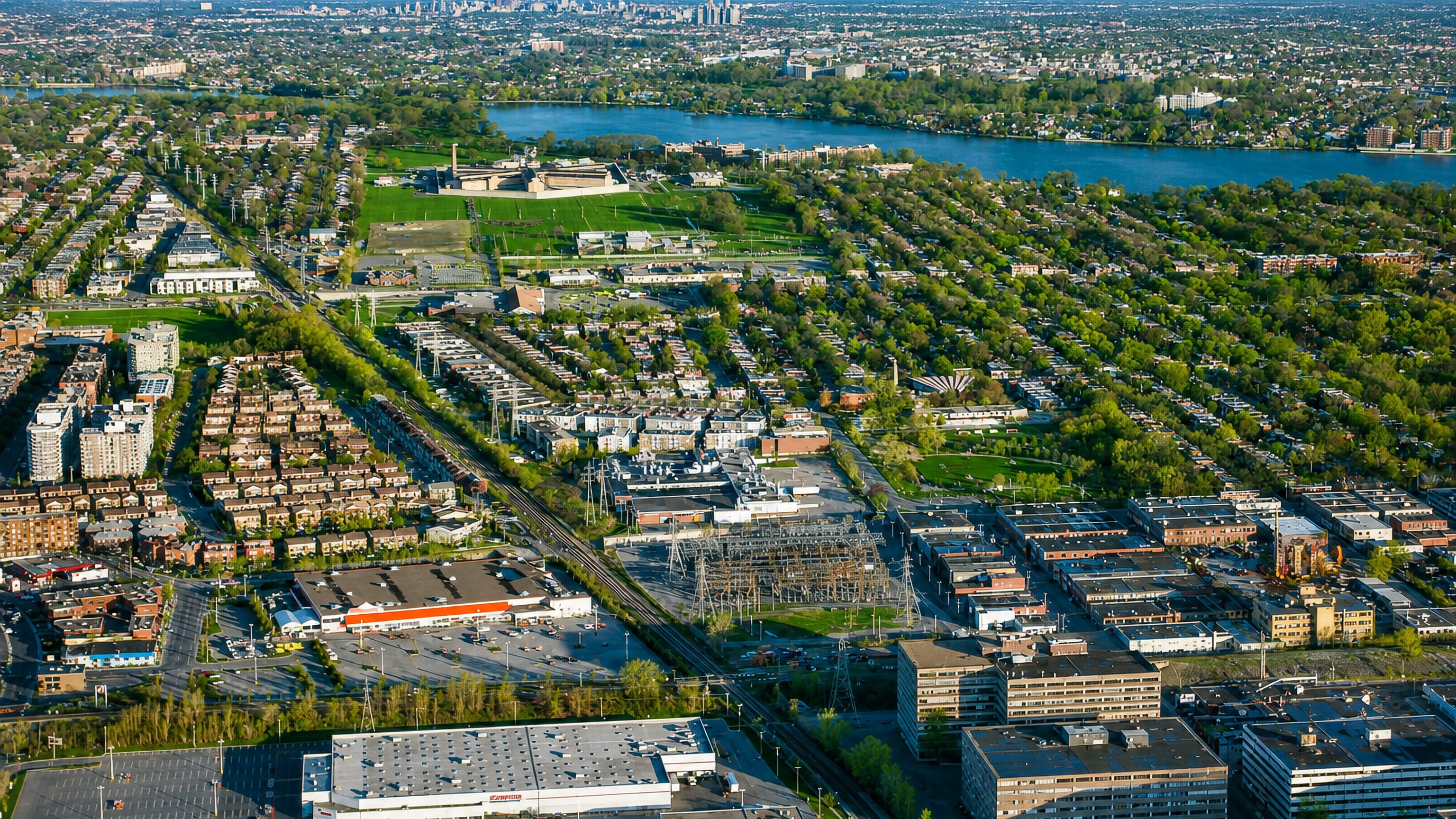 Aerial view over Ahuntsic-Cartierville's residential streets in Montreal, with the Riviere des Prairies and the distant downtown skyline.