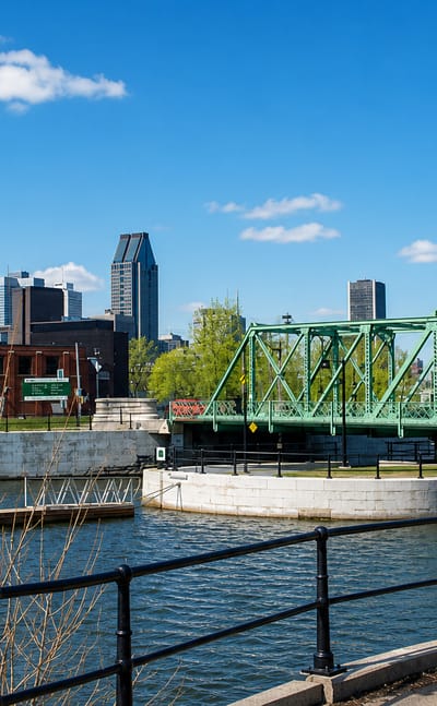 The Lachine Canal in Petite-Bourgogne, Montreal, with a green swing bridge and the downtown skyline beyond.