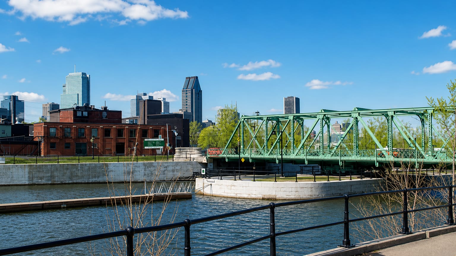 The Lachine Canal in Petite-Bourgogne, Montreal, with a green swing bridge and the downtown skyline beyond.