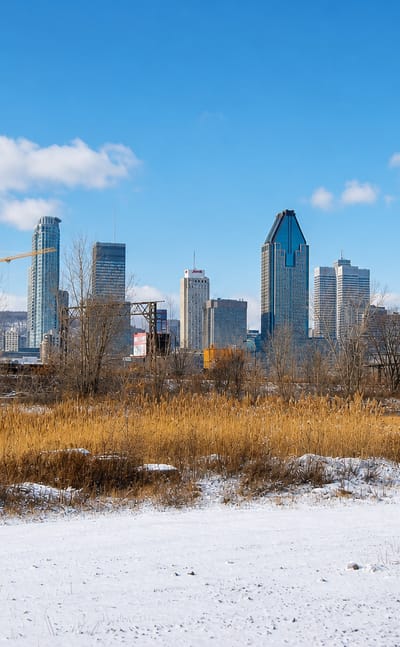 Montreal's downtown skyline seen across the snow-covered open land of Pointe-Saint-Charles with rail cars.