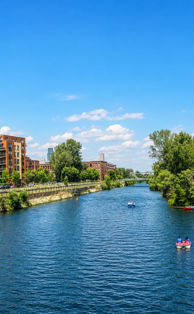 The Lachine Canal in Saint-Henri, Montreal, lined with brick residential buildings and pedal boats on the water.