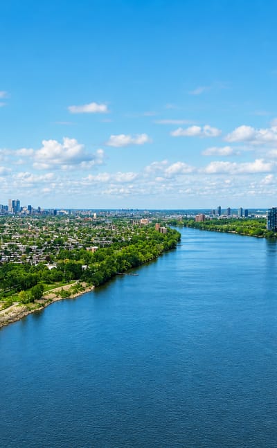 The St. Lawrence River with green wooded banks and the distant Montreal skyline seen from Verdun