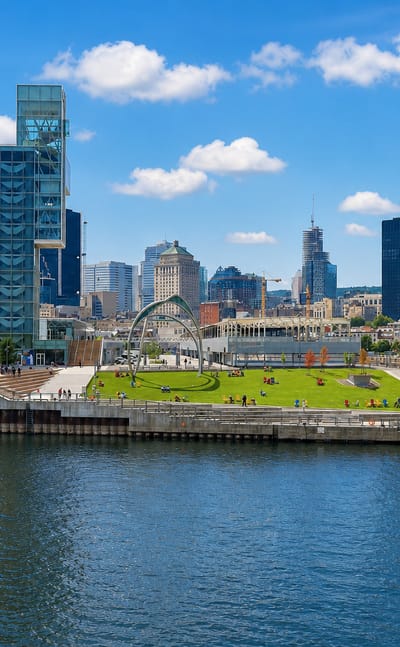 Old Montreal's Old Port waterfront with a grassy pier and the downtown skyline rising behind the river.