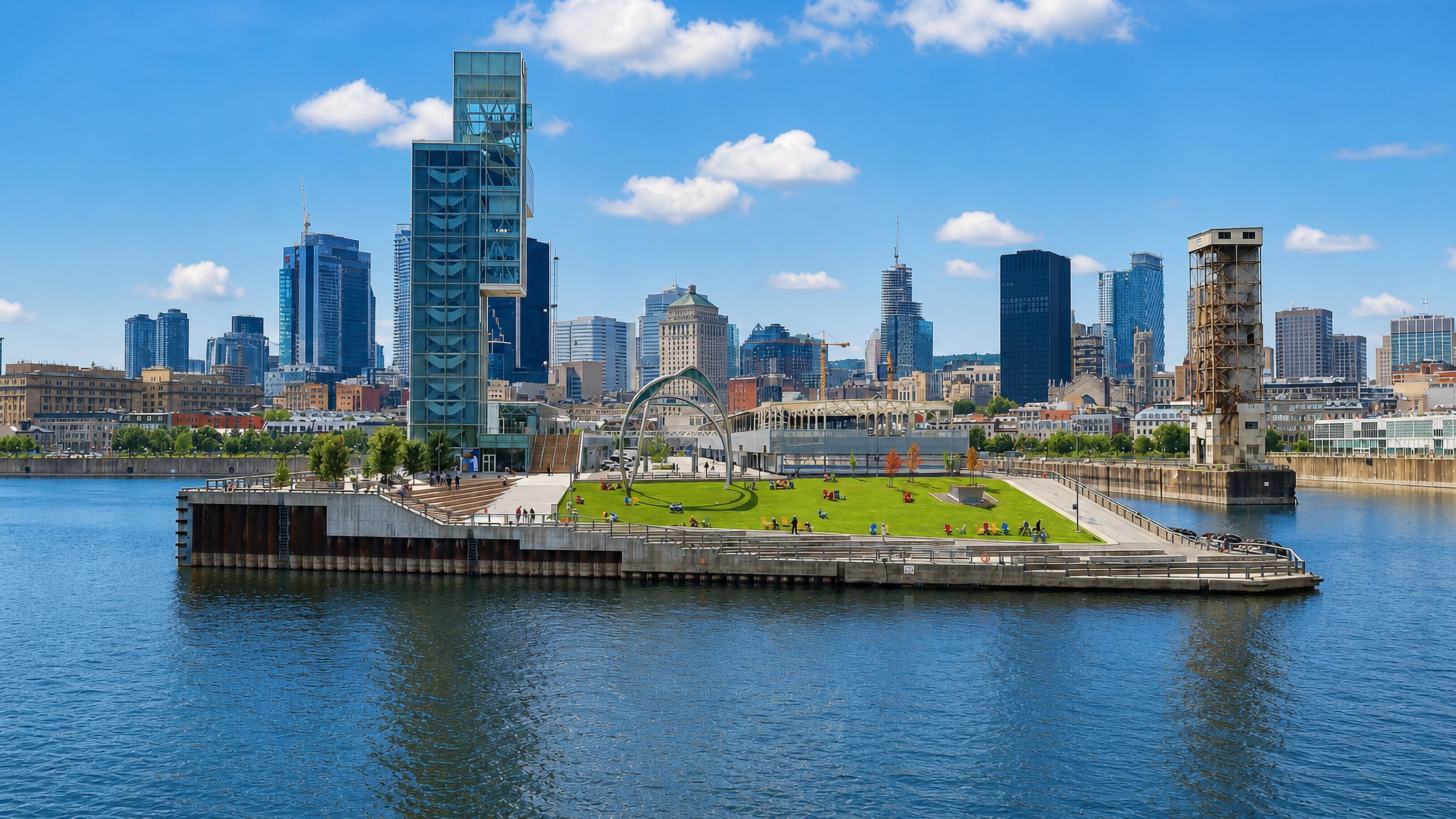 Old Montreal's Old Port waterfront with a grassy pier and the downtown skyline rising behind the river.