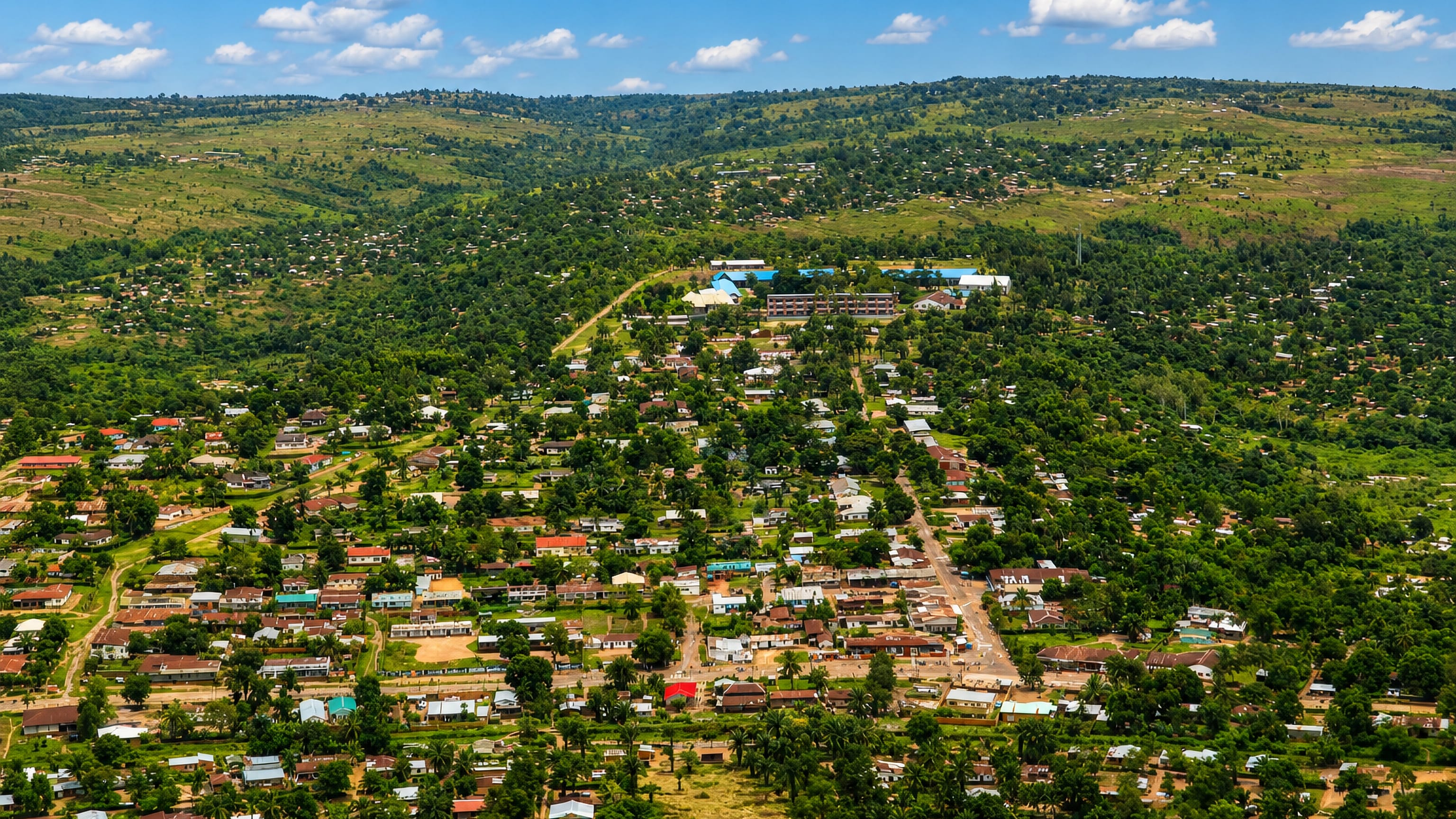 Aerial view of Kananga's low-rise, tree-shaded neighbourhoods spreading across green hills in DR Congo.
