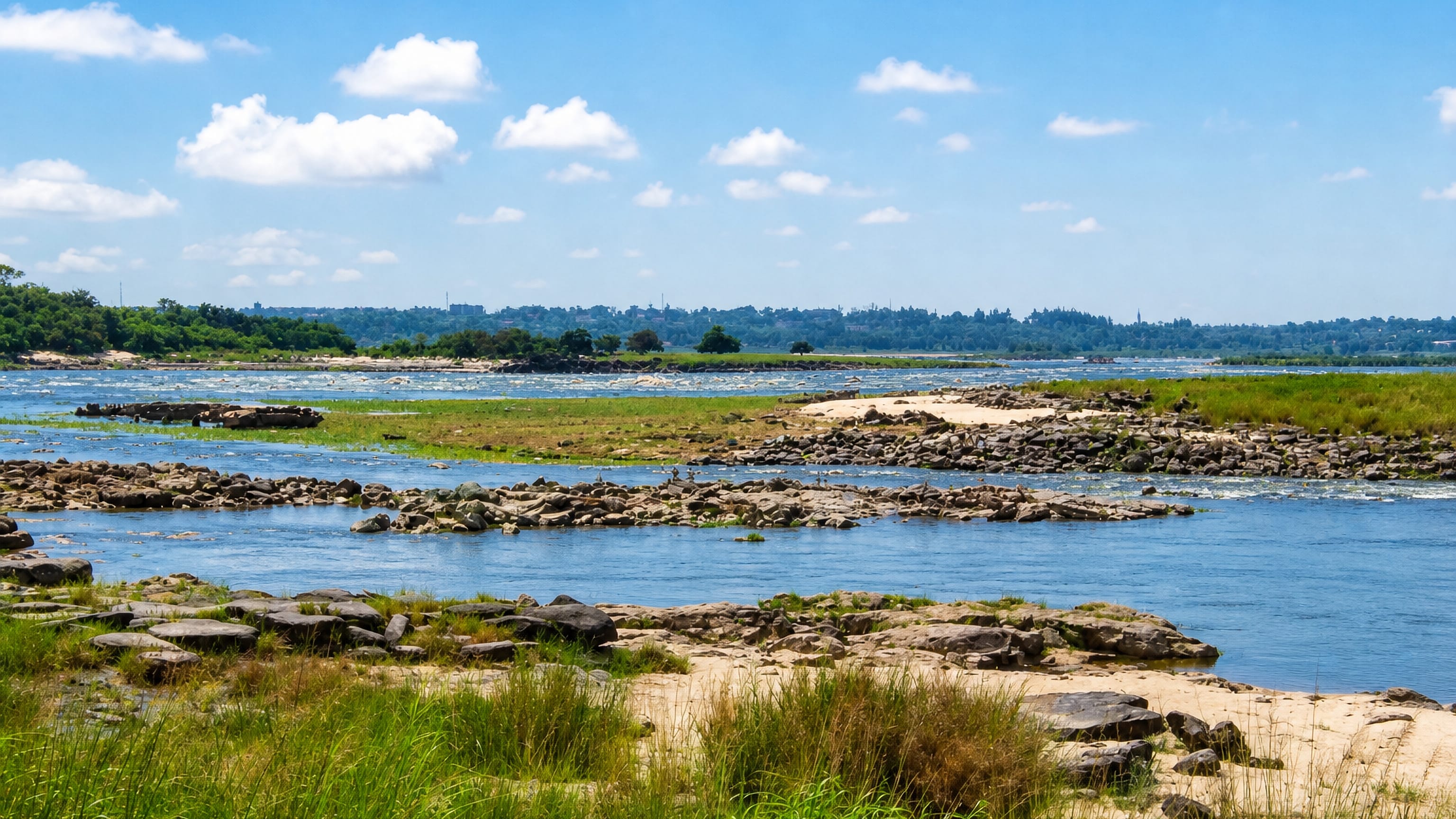 Rocky rapids on the Congo River beside Ngaliema in Kinshasa, with the city's low skyline on the far bank.