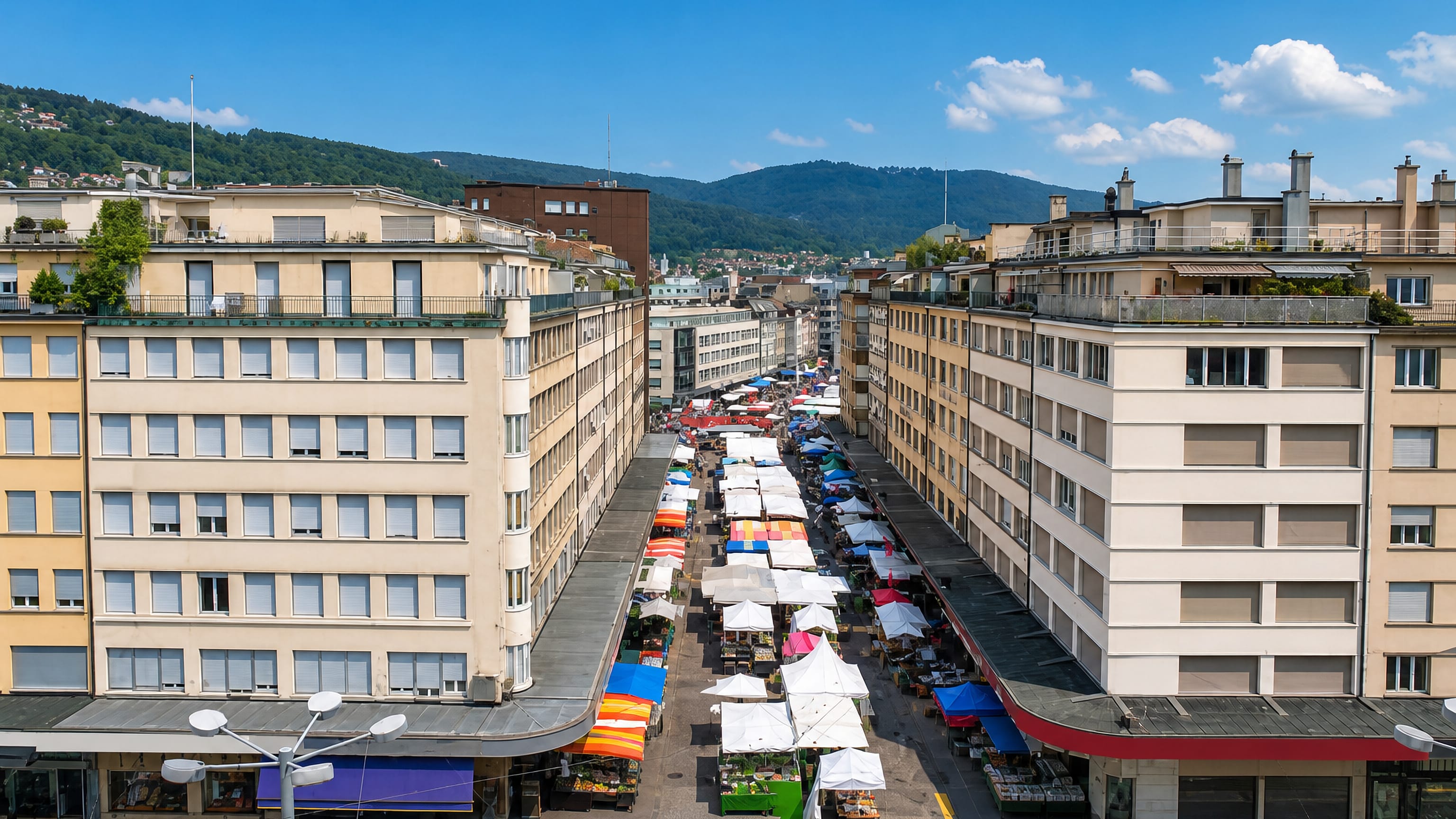 Colourful market stalls filling a Biel/Bienne street between 1930s modernist blocks, with Jura hills behind.