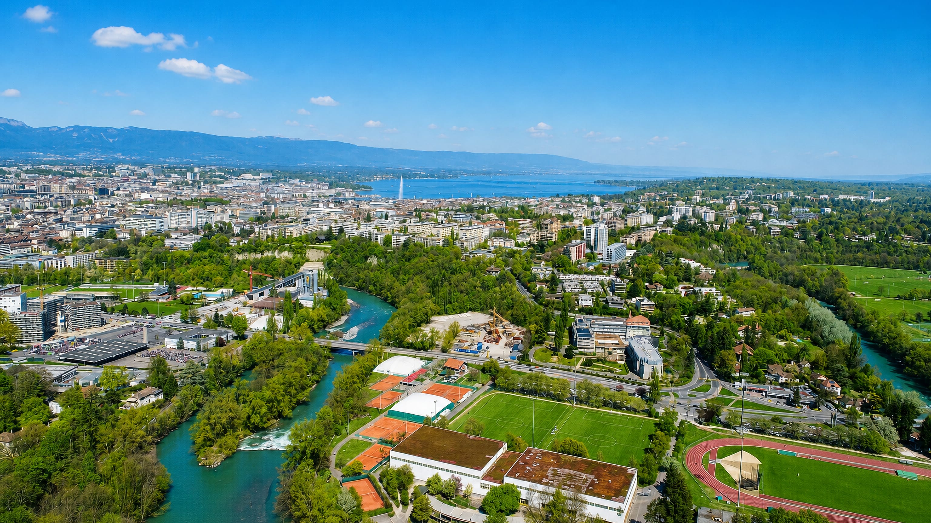 Aerial view of Geneva's Champel district above the Arve, with sports fields, the lake and the Jet d'Eau beyond.