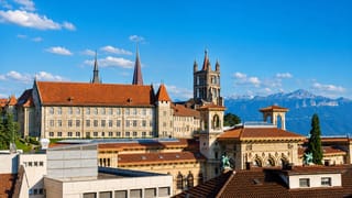Lausanne's Gothic cathedral tower and the Palais de Rumine above old-town rooftops, with the Alps beyond