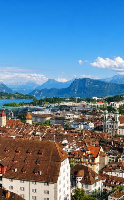 Panorama of Lucerne, Switzerland, over the old town's red rooftops toward the lake and snow-tinged Alps.