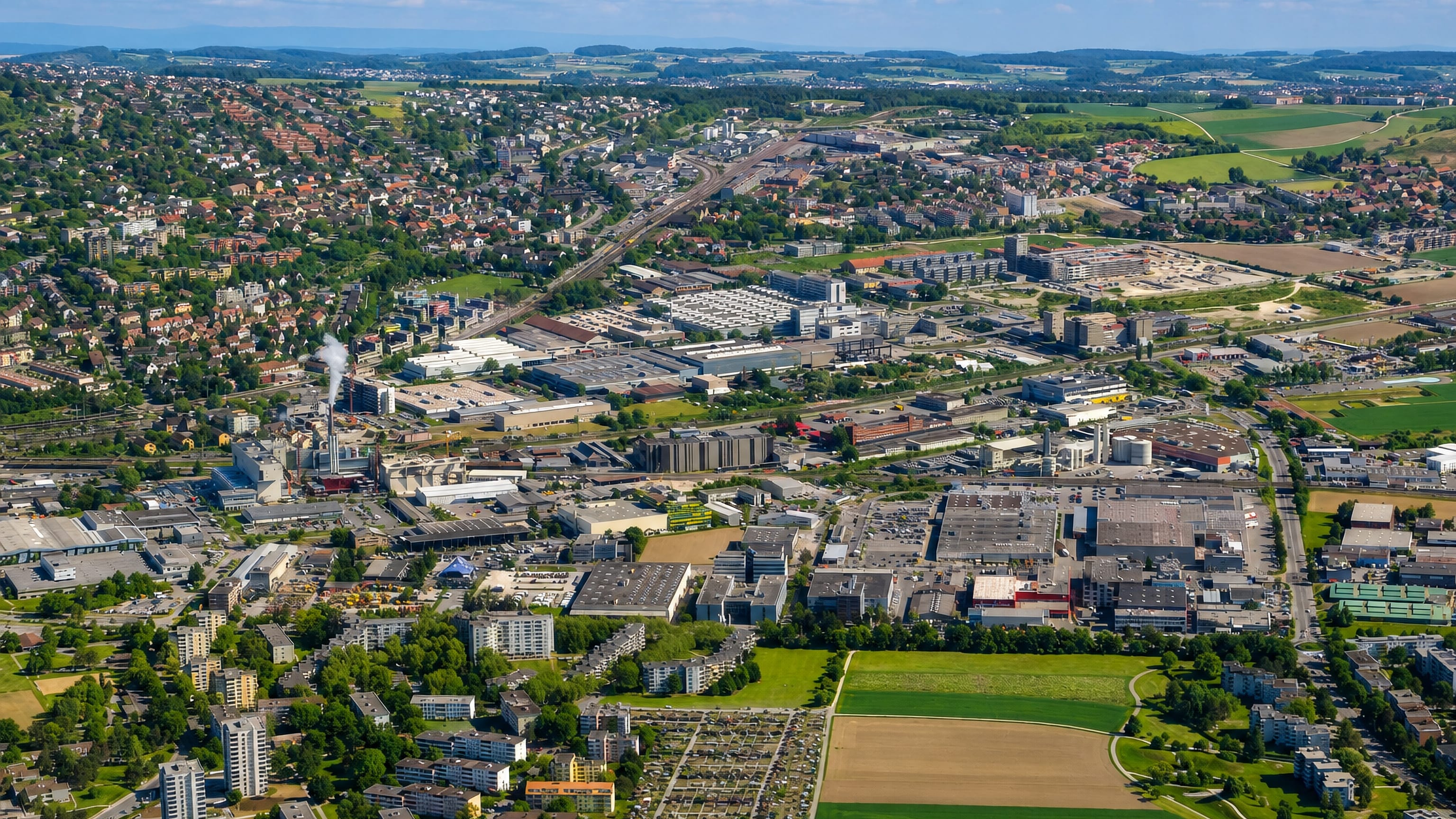 Aerial view over the Grüze area of Oberwinterthur in Winterthur, with industrial estates, rail lines and wooded hills.