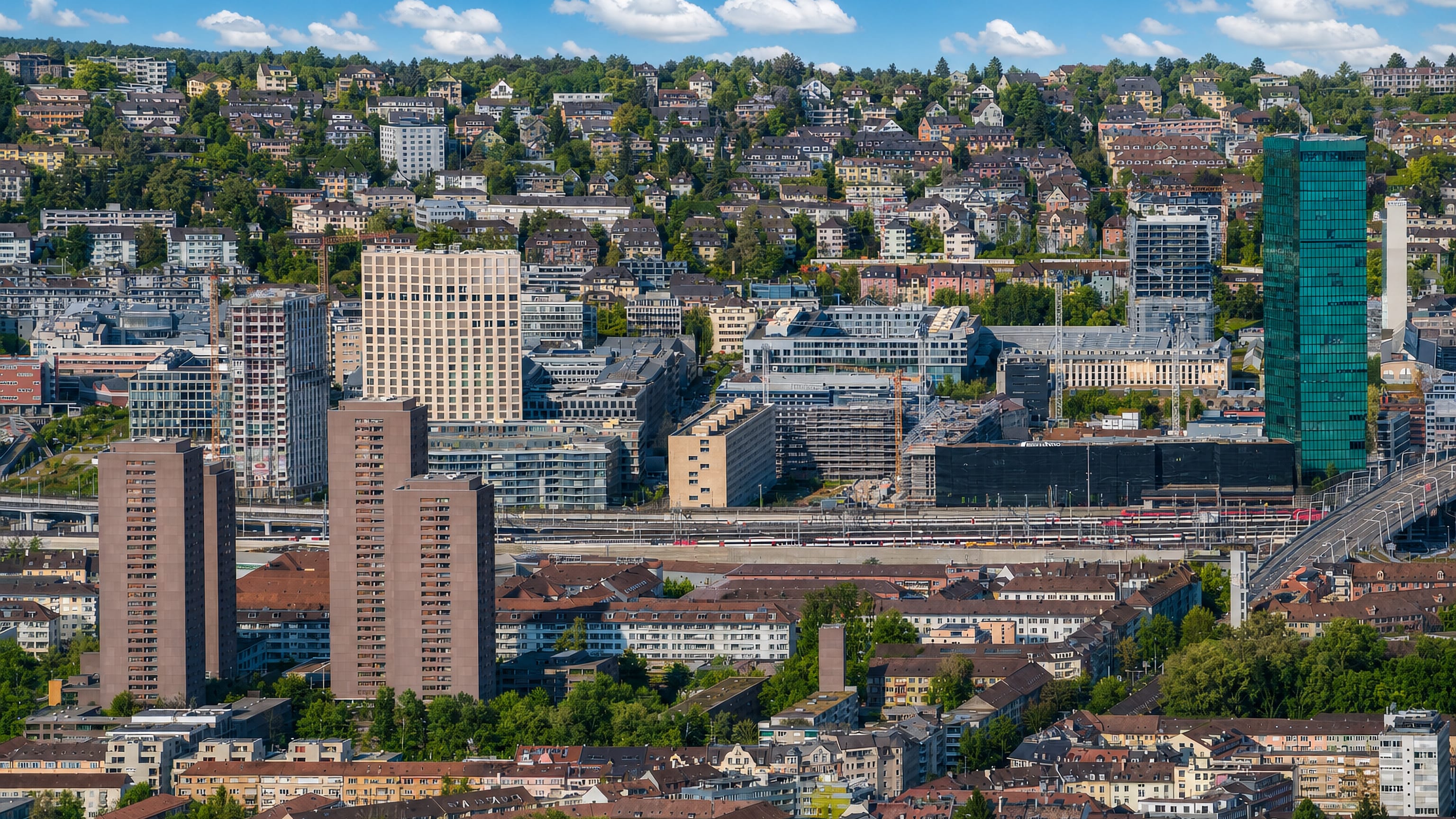 Aerial view over Zurich's Hard quarter in Kreis 4, with the green Prime Tower and rail corridor below wooded hillsides