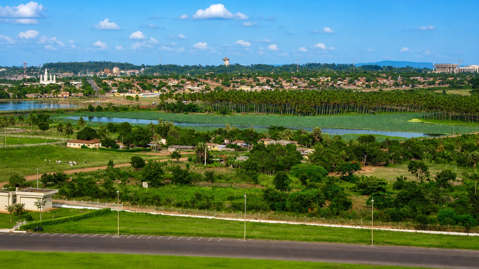 Yamoussoukro, Ivory Coast, green landscape with a lake and the distant basilica beyond palm groves.