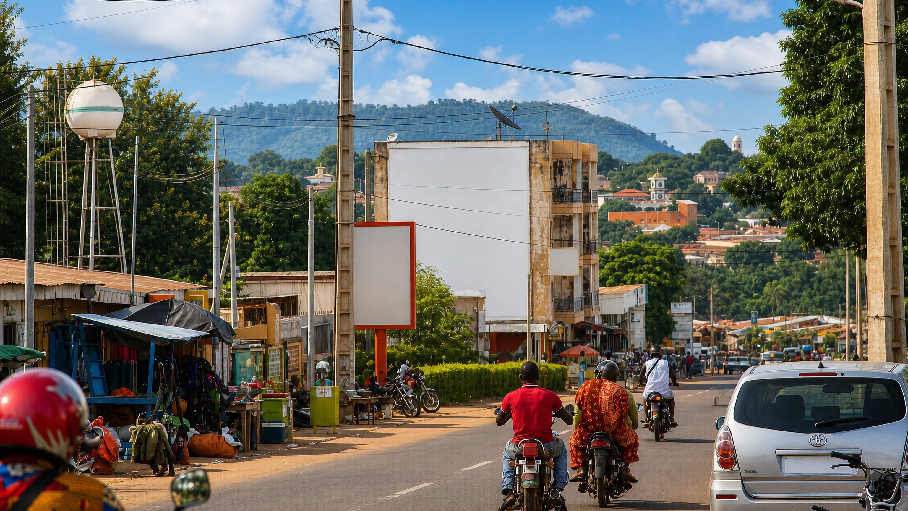 Motorbikes and roadside stalls on a main street in Korhogo, northern Cote d'Ivoire, with green hills behind.
