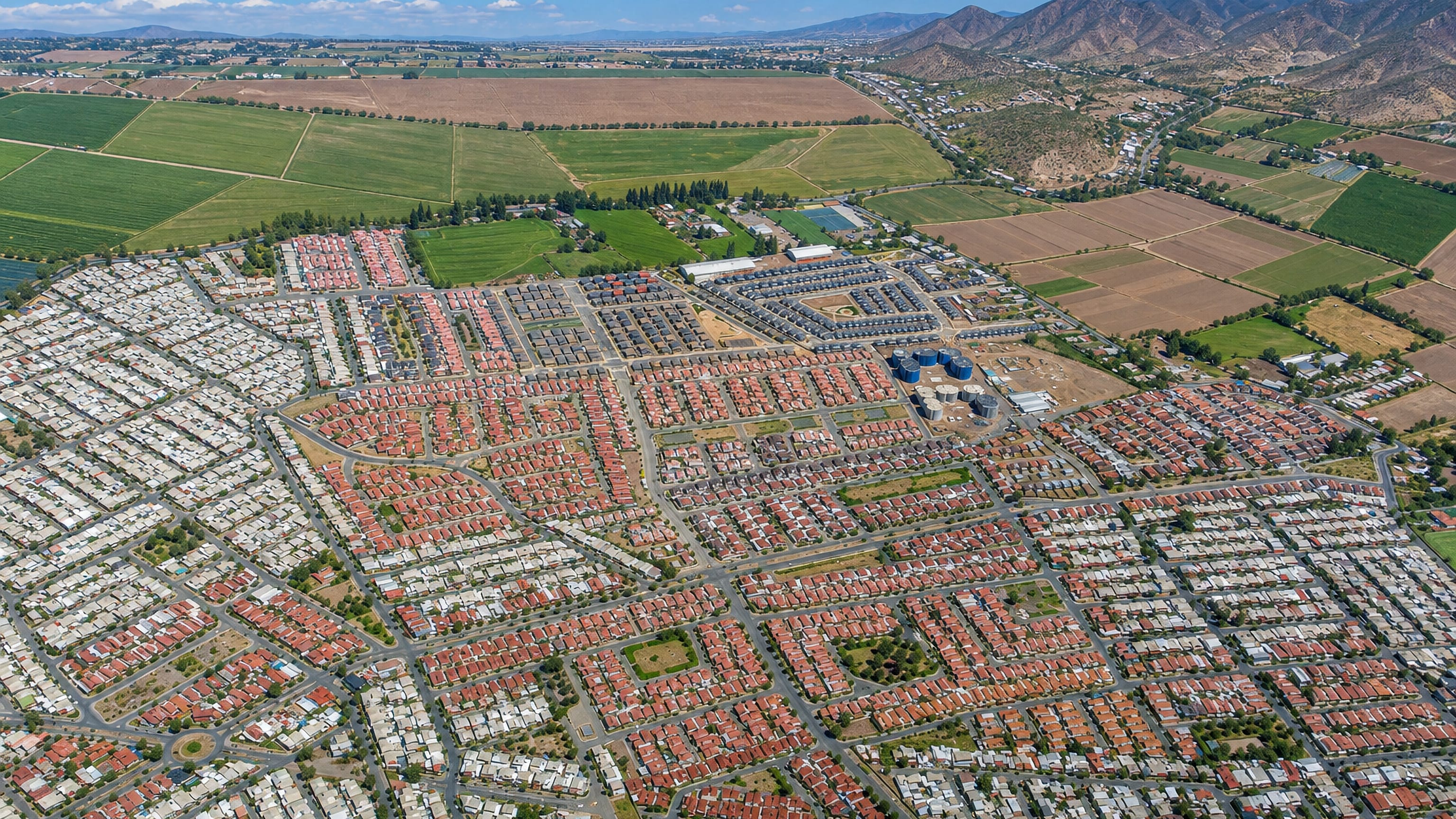 Aerial view of Los Andes, Chile, with red-roofed housing grids meeting farm fields and Andean foothills.