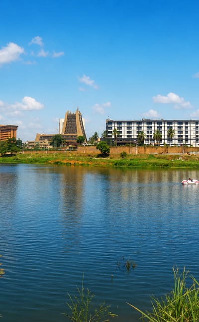 Yaounde's Municipal Lake with the city skyline and a tent-roofed landmark building rising behind green banks