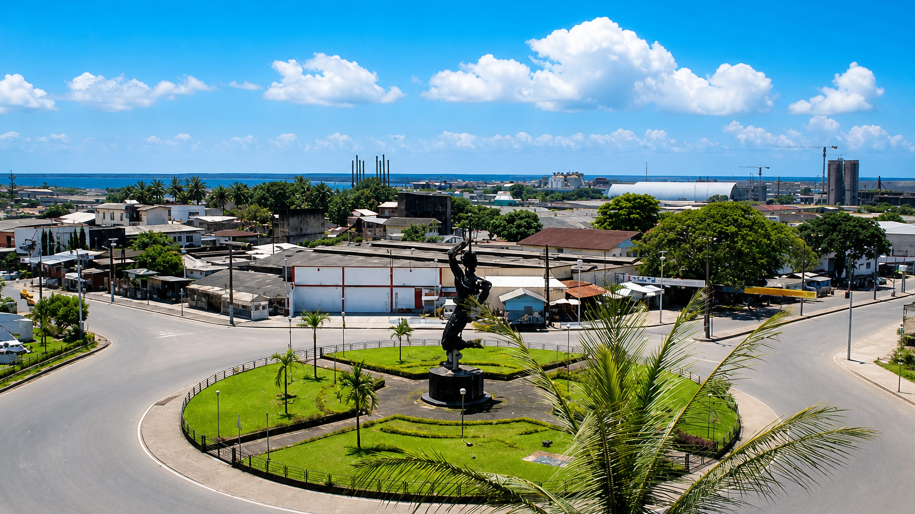 Douala, Cameroon: a landscaped traffic roundabout with a bronze statue, port warehouses and the estuary beyond.