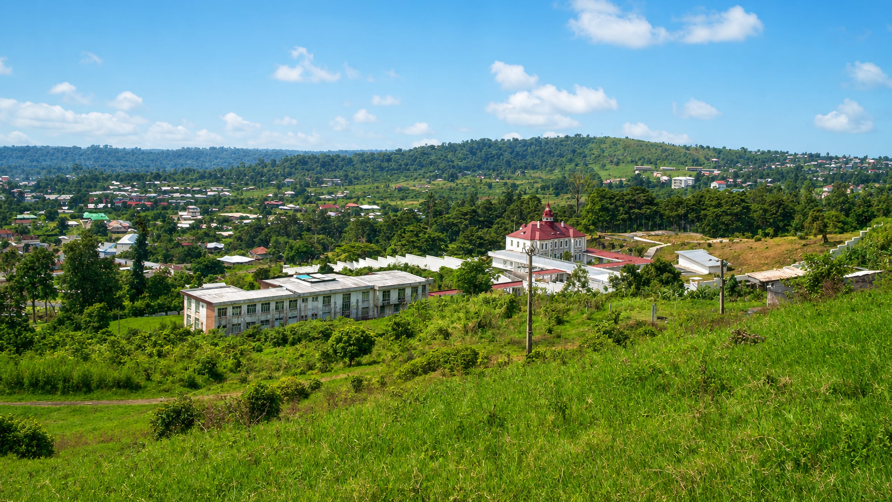 Green hills above Buea, Cameroon, with a red-roofed colonial building and tin-roofed houses among the trees.