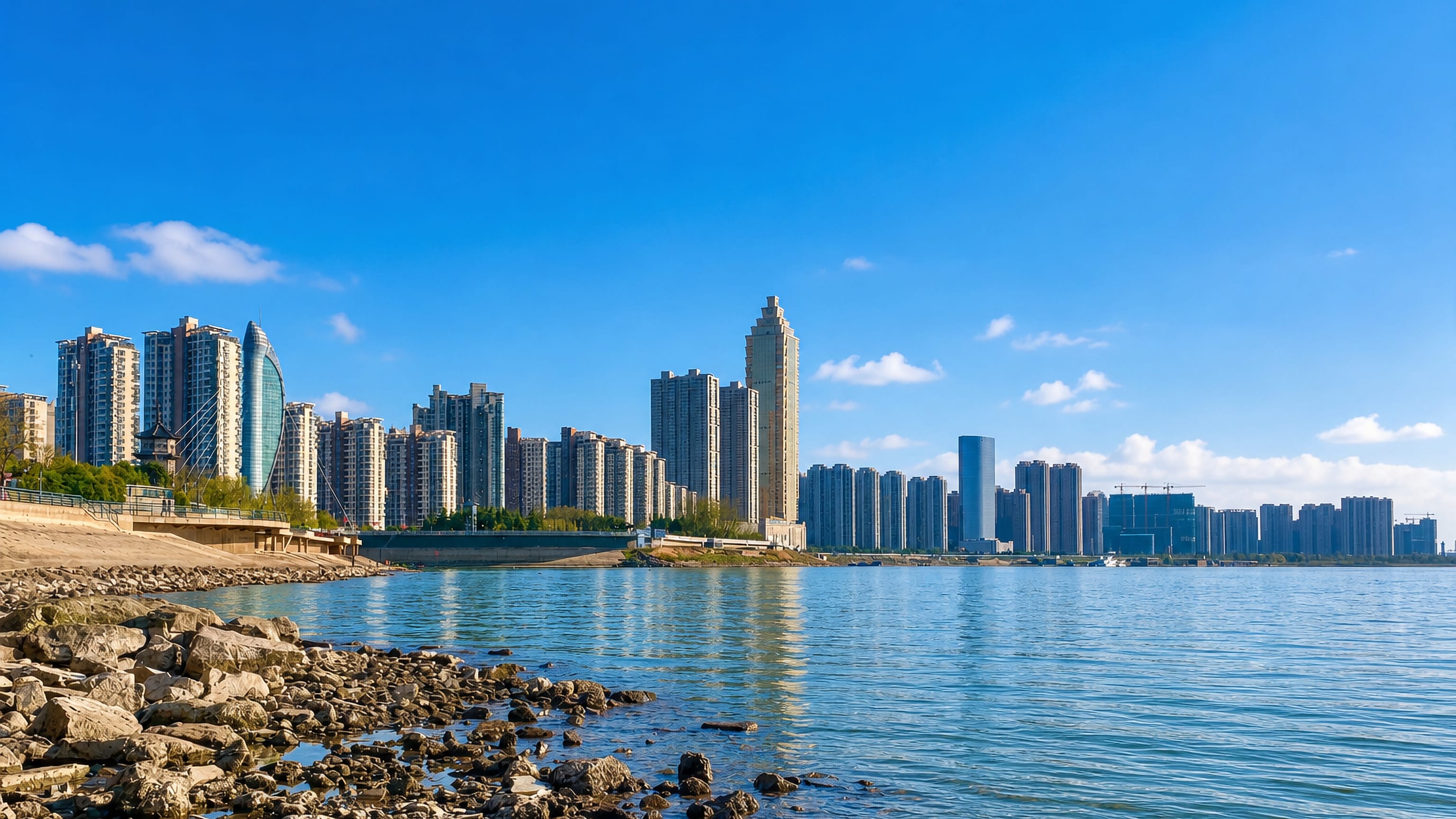 Wuhu's high-rise riverfront and riverside pagoda seen across the Yangtze from a rocky shore