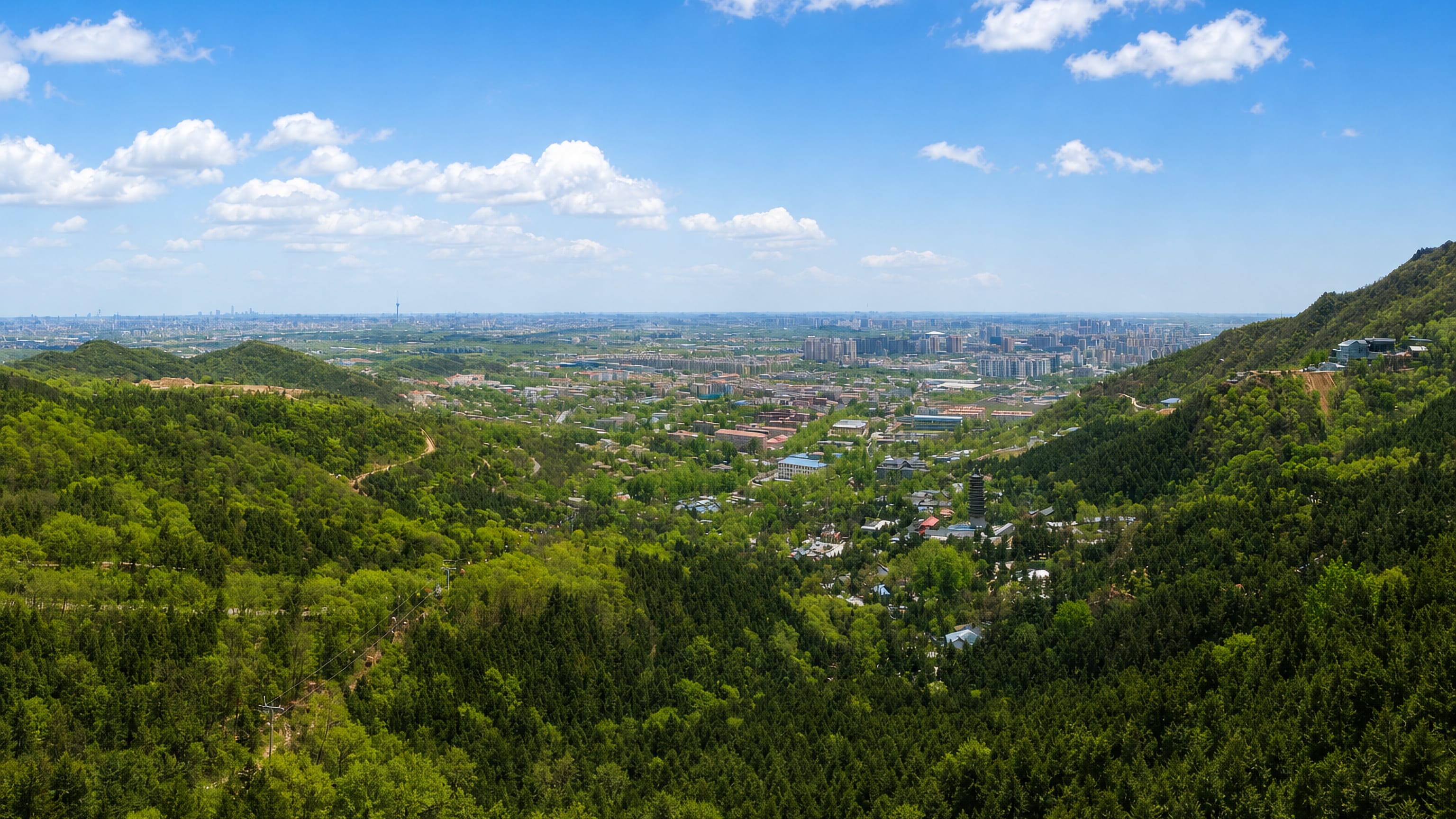 Forested Western Hills of Mentougou District framing a valley town and Beijing's distant skyline.
