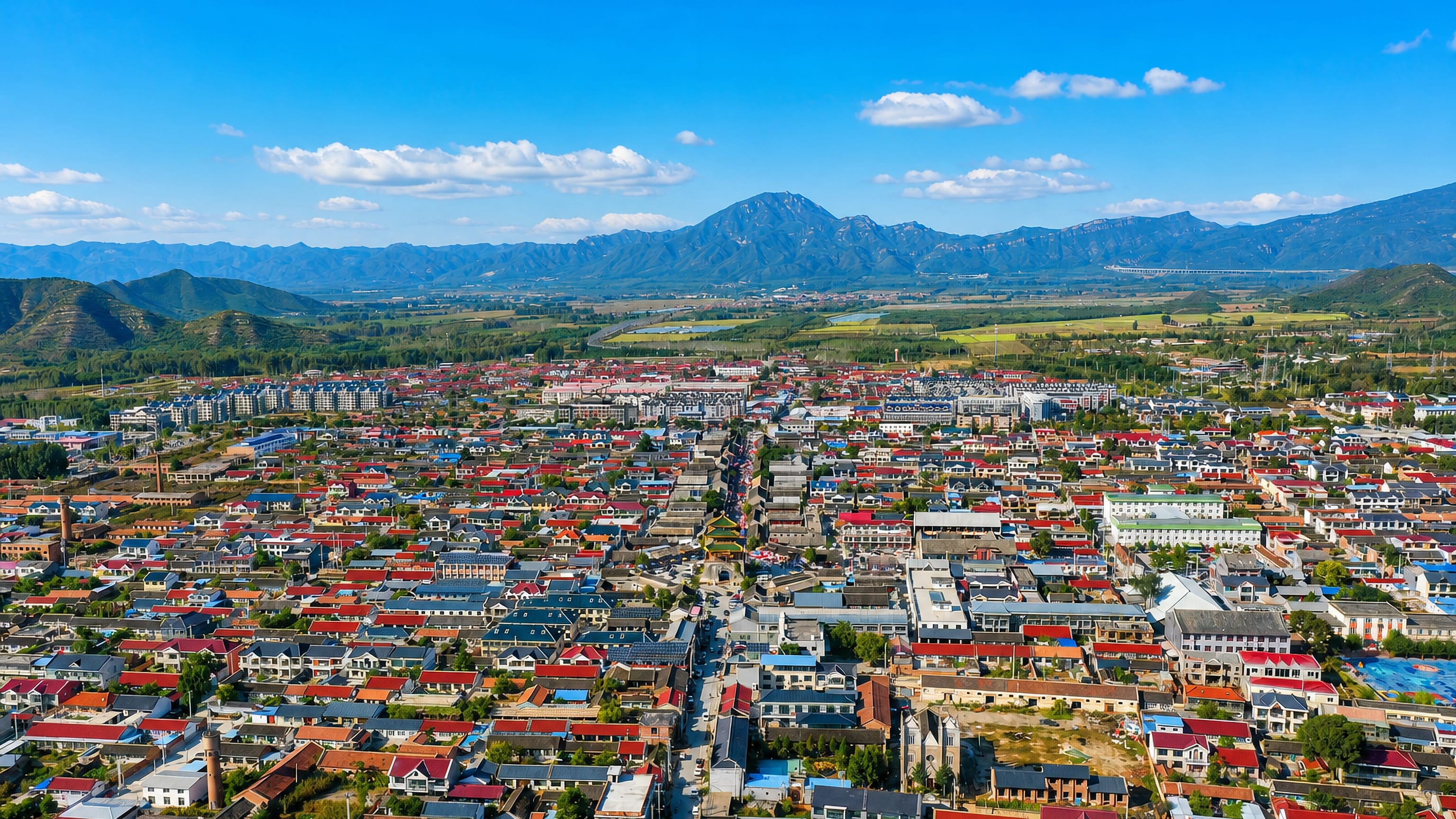 Aerial view over Yanqing District's low-rise red-roofed town centre with mountain ridges rising north of Beijing.