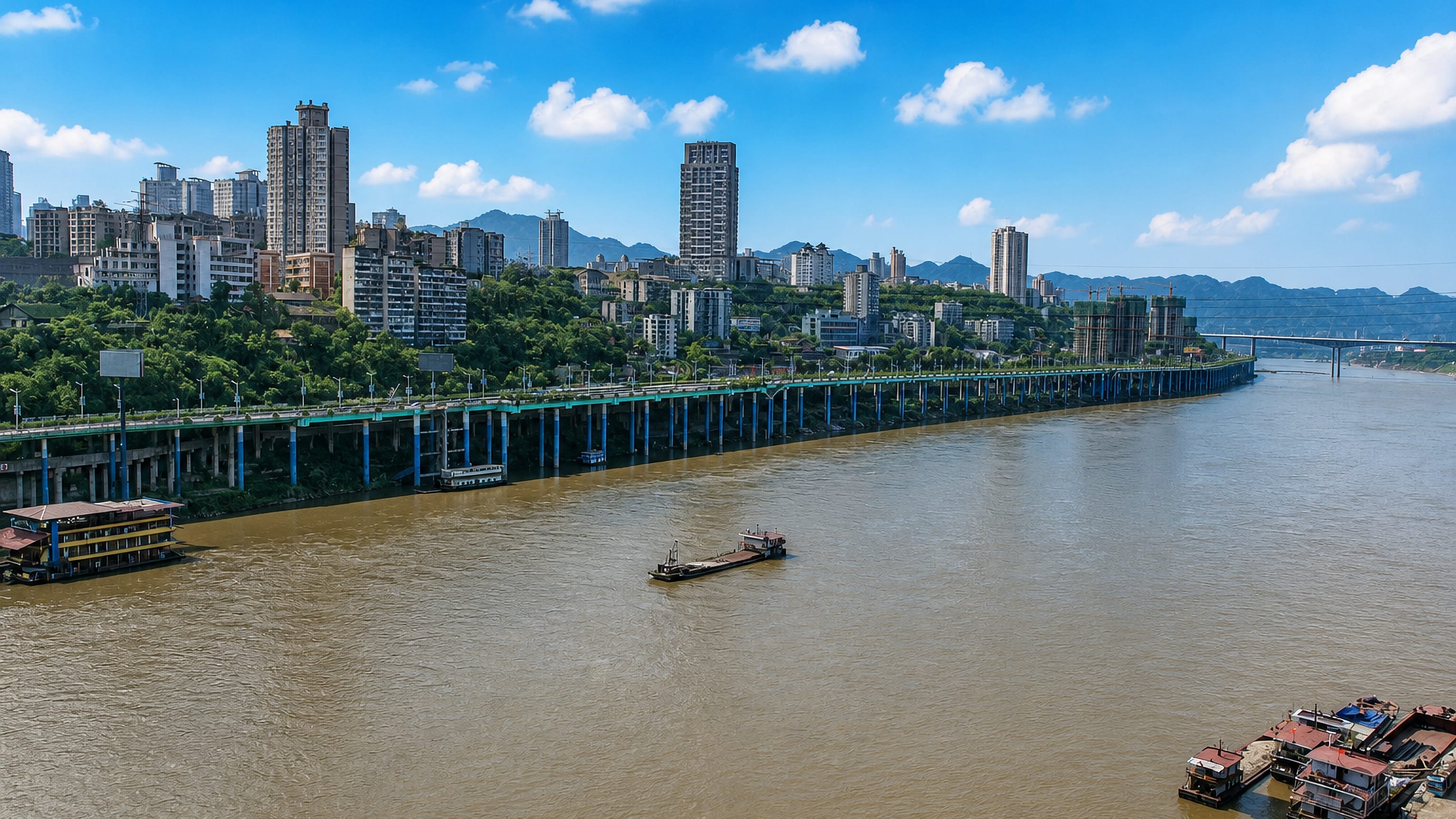 High-rises on wooded hillsides above the Jialing River and its elevated riverside road in Shapingba, Chongqing.