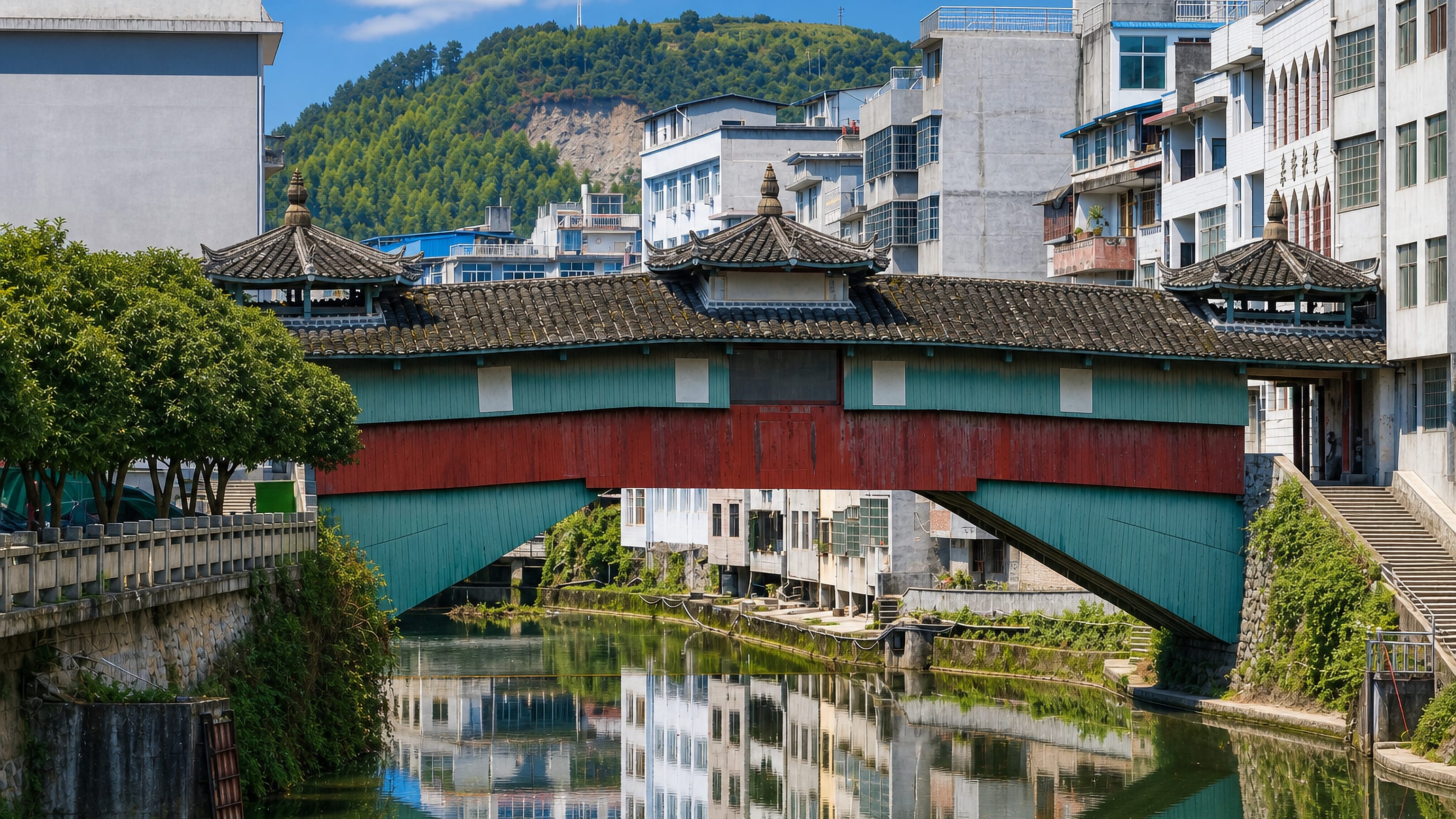 A tiled covered wooden bridge with pavilions spanning a canal below wooded hills in Ningde, Fujian.