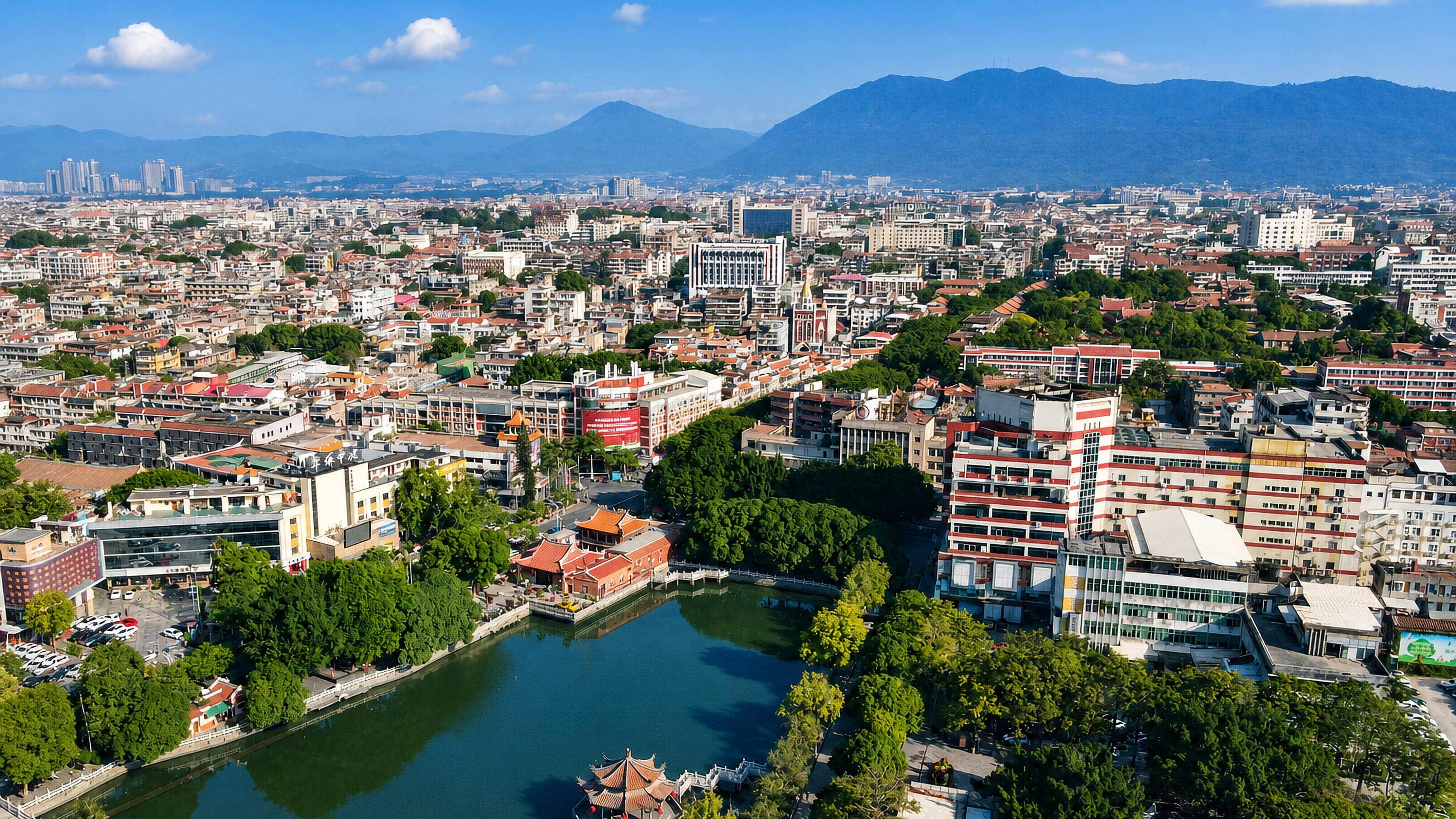 Aerial view over Quanzhou, Fujian: a lakeside pavilion, red-tiled low-rise streets and hazy mountains beyond.