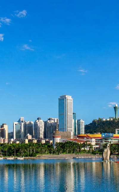 Palm-lined waterfront and high-rise skyline of Xiamen reflected in calm water below a hilltop tower.