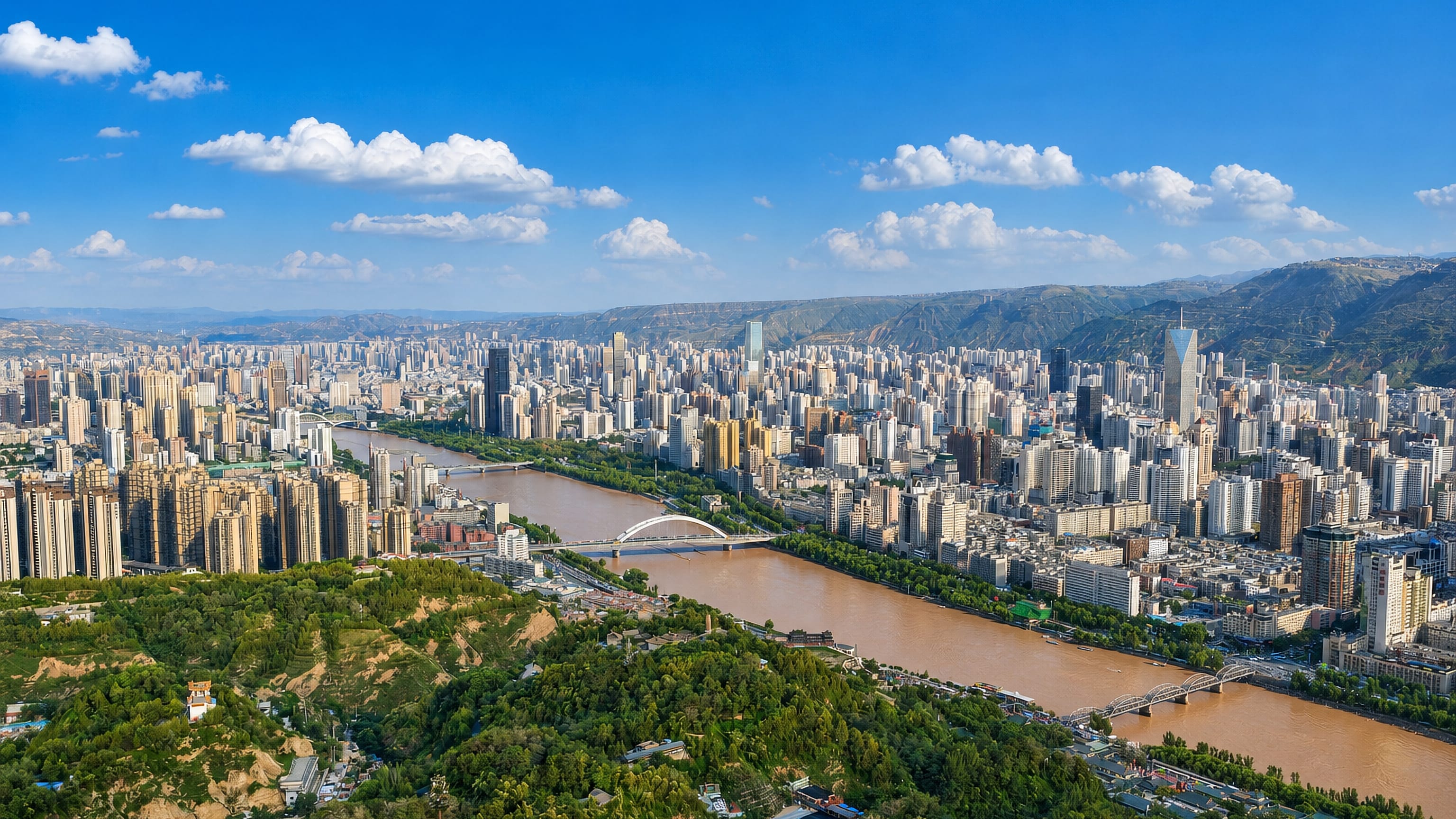 Lanzhou's high-rises line the muddy Yellow River between arid hills, crossed by arch bridges.