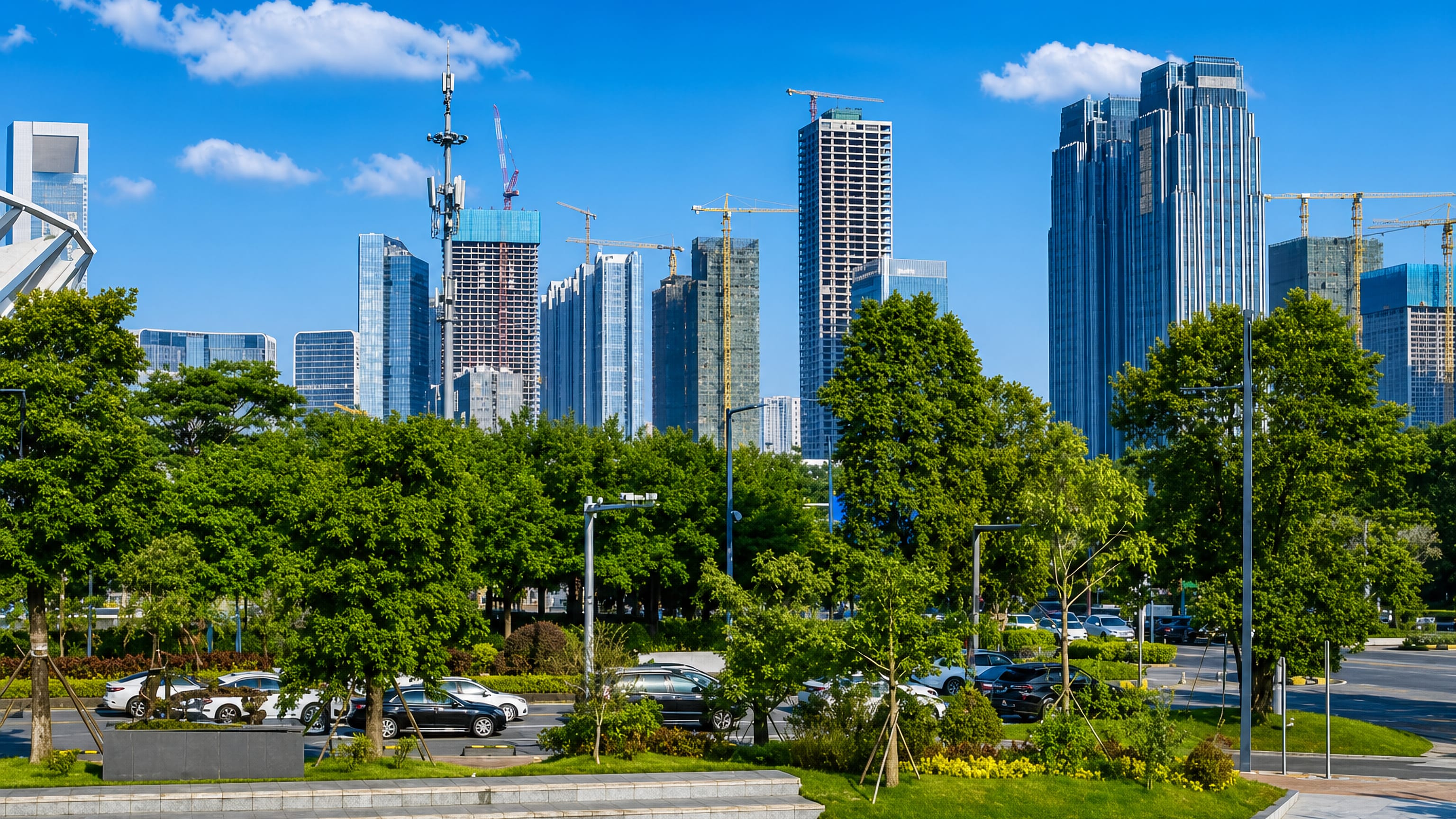 Foshan's glass high-rises and construction cranes rising above a tree-lined city park in Guangdong, China.