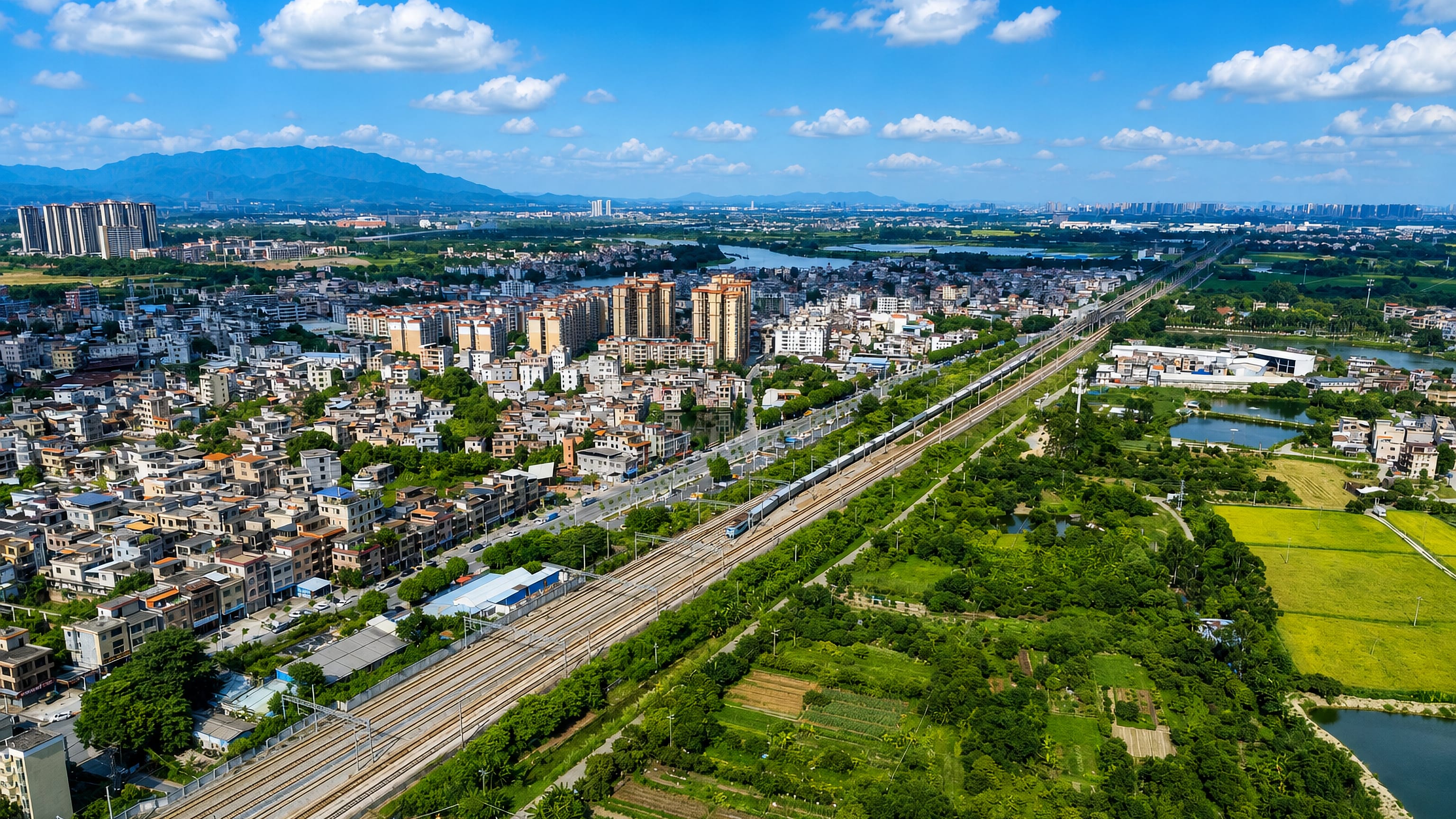 Aerial view of Zengcheng District, Guangzhou, with a rail corridor cutting between farmland, villages and apartment blocks.