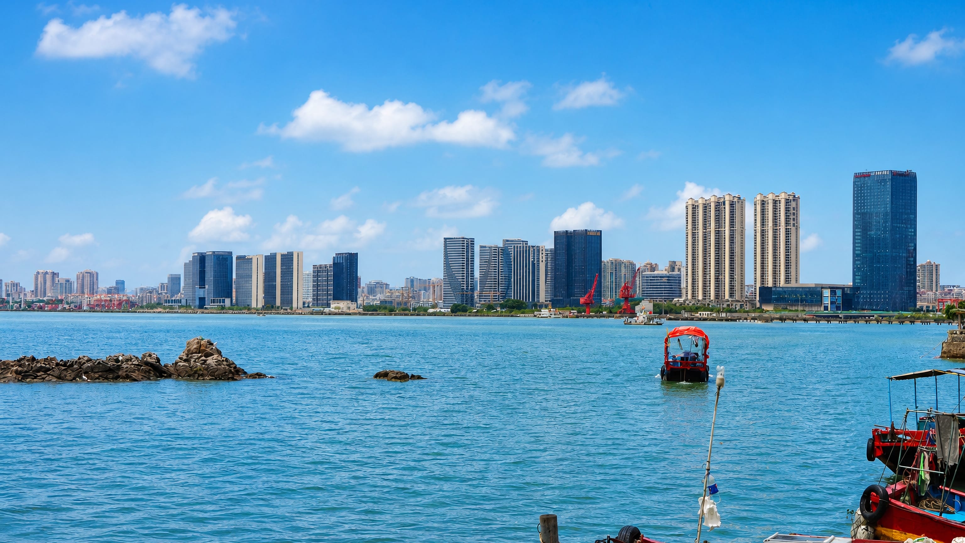 Shantou's waterfront high-rises across the bay with red-hulled fishing boats moored in the foreground