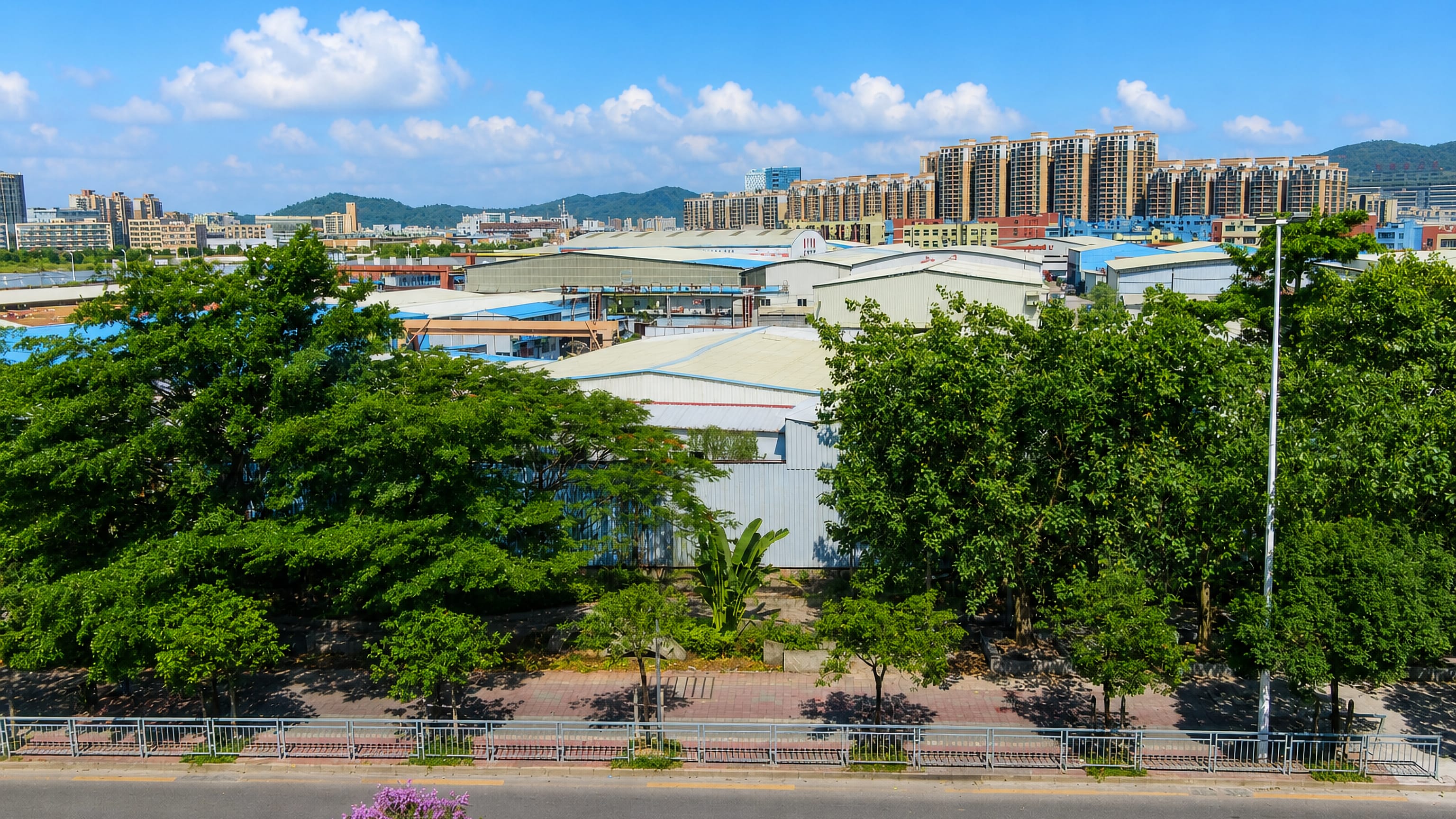 Warehouses, a tree-lined road and mid-rise apartment blocks in Bao'an District, Shenzhen, with green hills behind