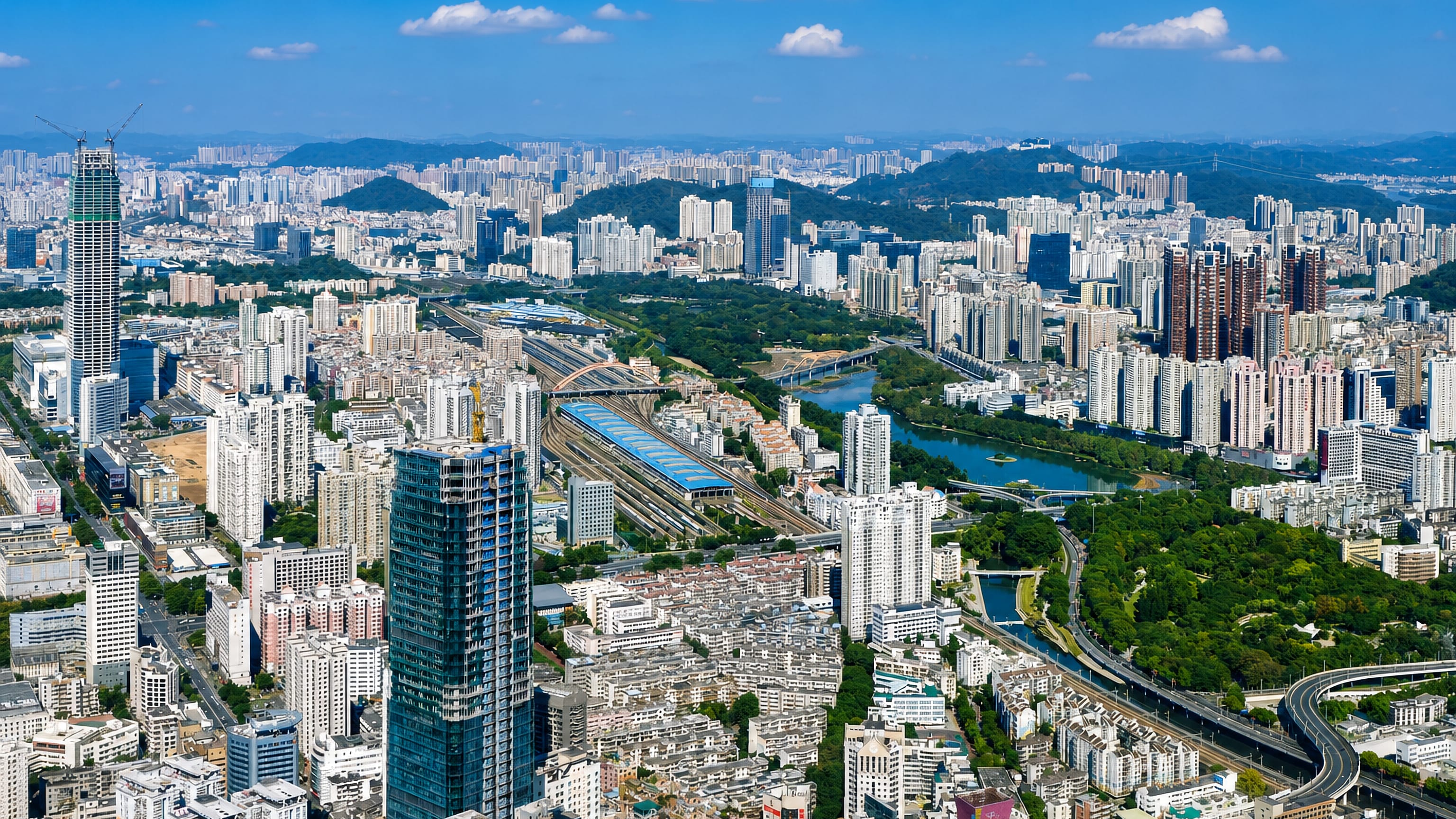 Longgang District, Shenzhen: dense high-rise blocks around a rail yard and river, with green hills beyond.