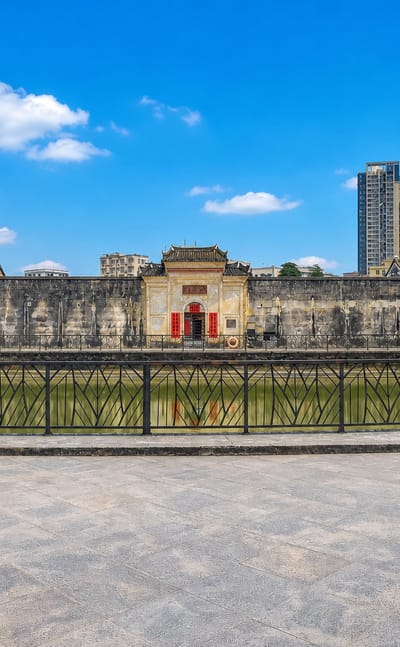 Historic walled ancestral hall with a decorated gatehouse fronting modern high-rise towers across water in Pingshan District, Shenzhen.