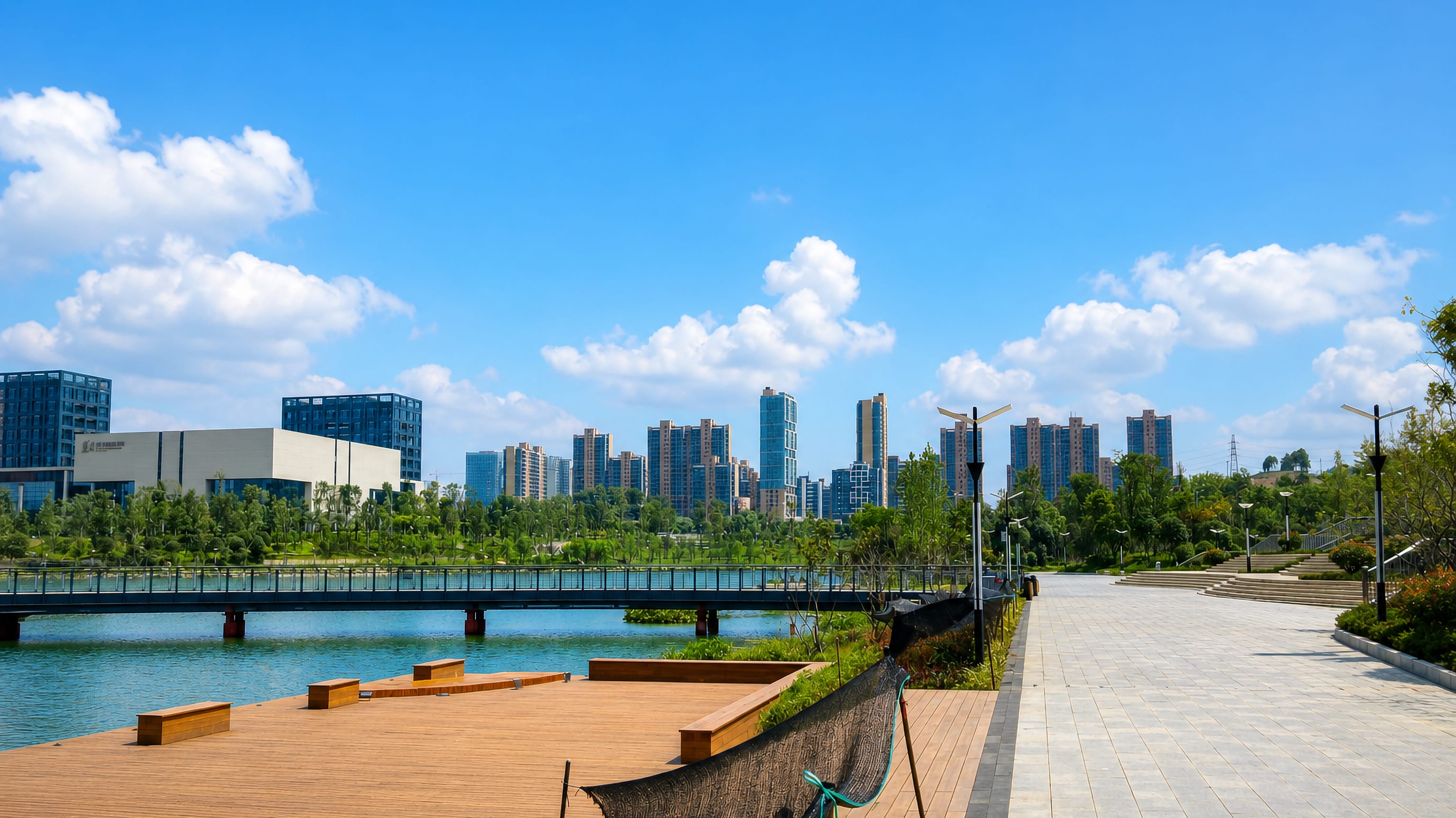 Riverside boardwalk park in Zunyi, Guizhou, with a footbridge and modern high-rise towers on the far bank.