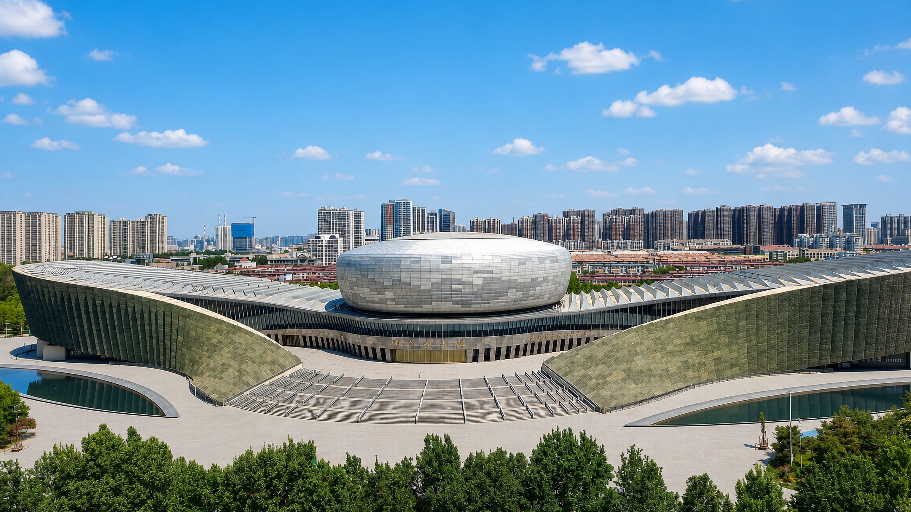 Elliptical steel-clad cultural centre with sweeping wings backed by high-rise housing in Handan, China.
