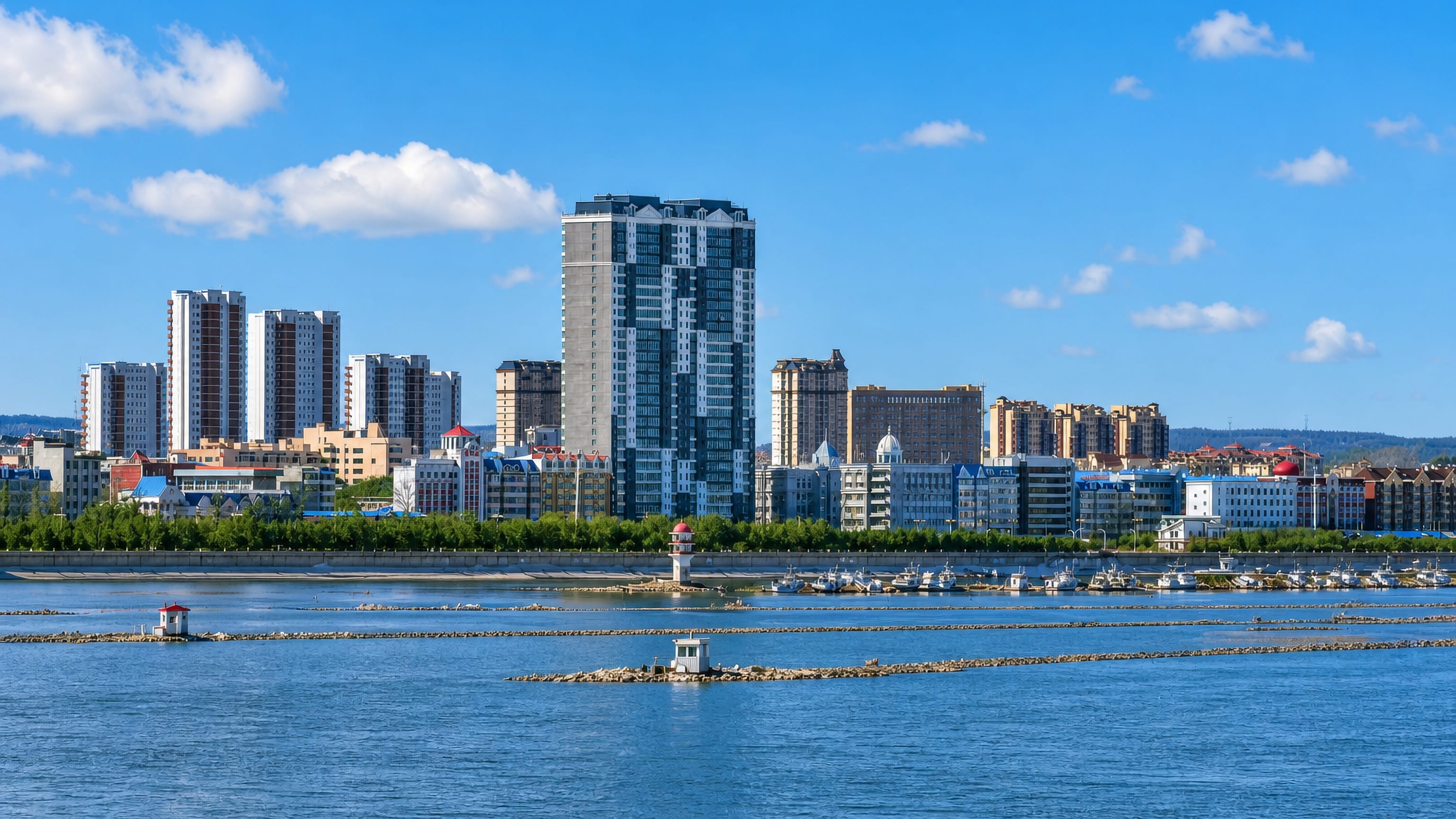 Heihe's riverfront skyline of apartment towers across the Amur River, with moored boats and breakwater beacons
