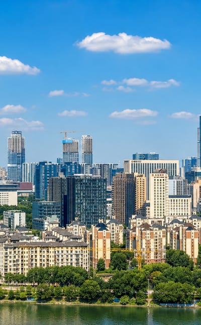 Riverside skyline of Zhengzhou with residential blocks and central high-rise towers under a blue sky.