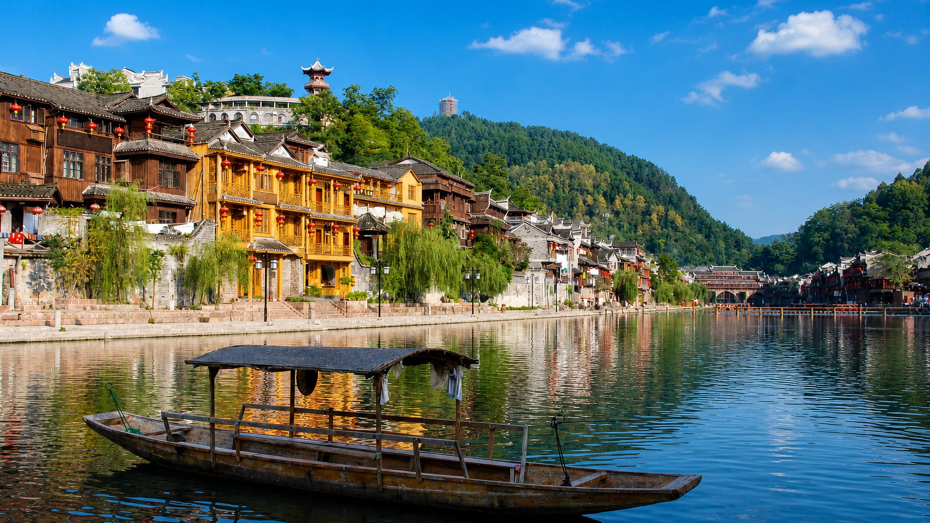 Wooden boat on the Tuojiang River below Fenghuang's stilted riverside houses and red lanterns, Hunan.