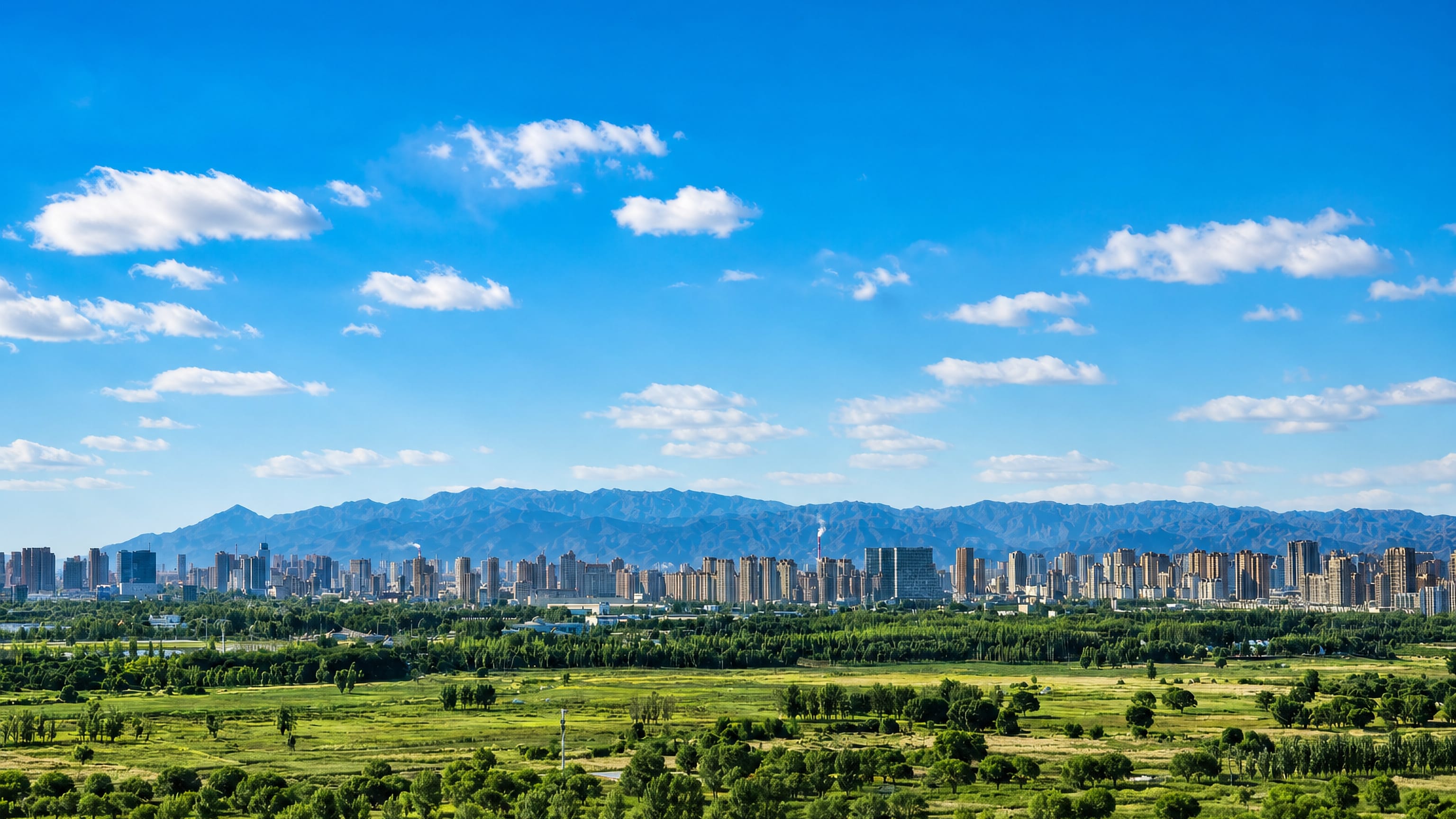 Wide skyline of Baotou, Inner Mongolia, with mountain ridges behind and green grassland spreading in front.