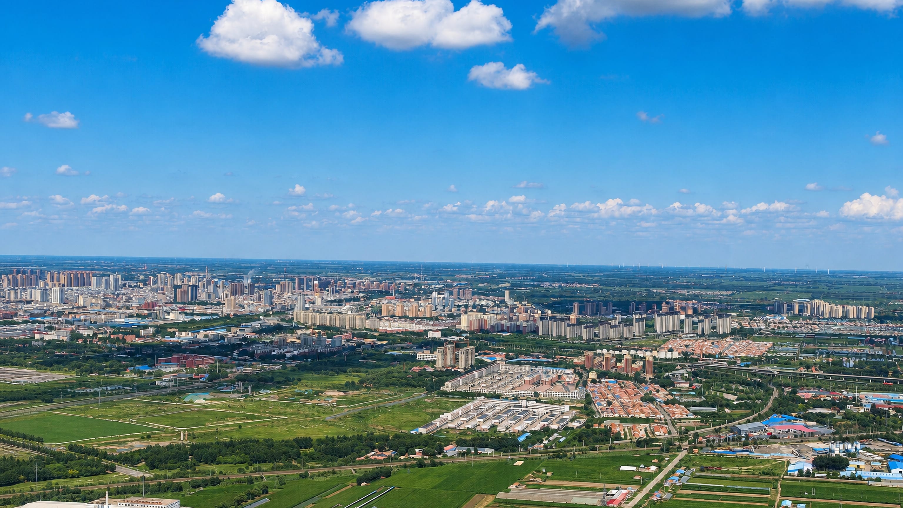 High aerial view of Tongliao, Inner Mongolia, where apartment blocks meet green farmland on the plains.