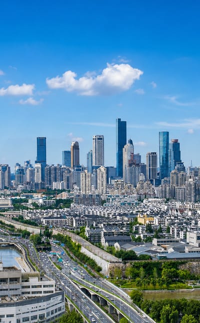 Nanjing skyline with the spired Zifeng Tower and a high-rise cluster above a canal and elevated highway