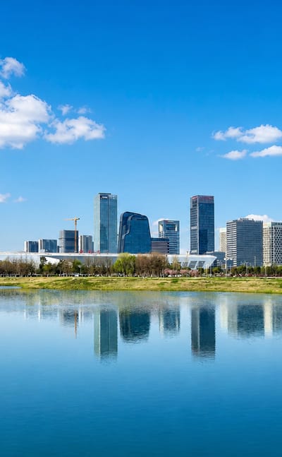 Modern lakeside skyline of Suzhou's business district mirrored in calm water under a blue sky.