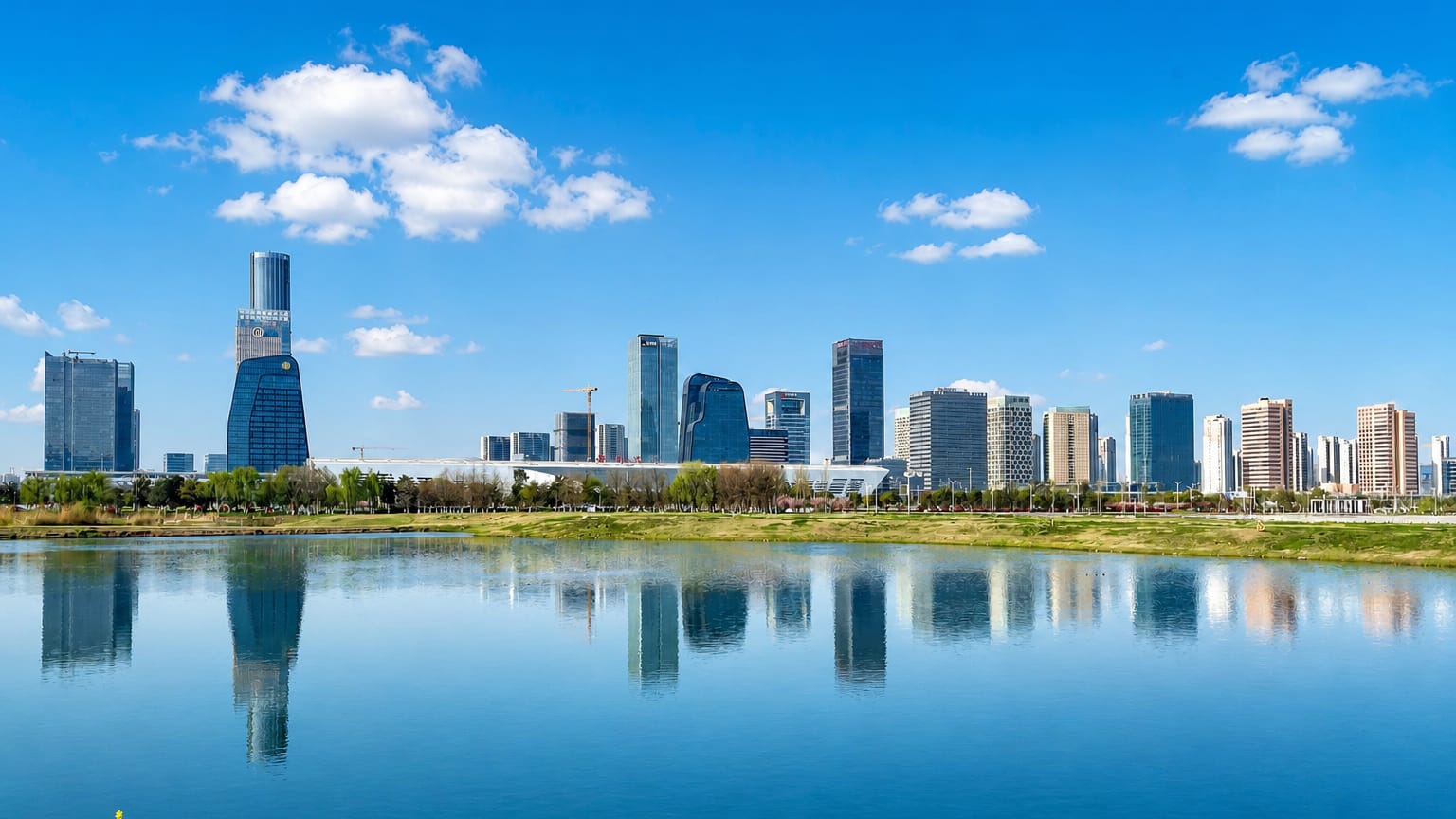 Modern lakeside skyline of Suzhou's business district mirrored in calm water under a blue sky.