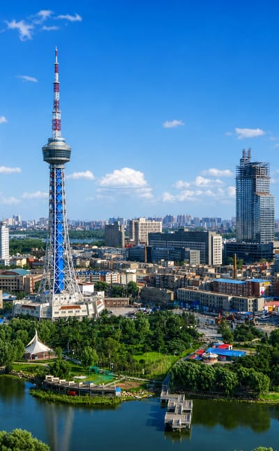 Changchun's lattice TV tower above a lakeside park and city skyline under a bright blue sky.