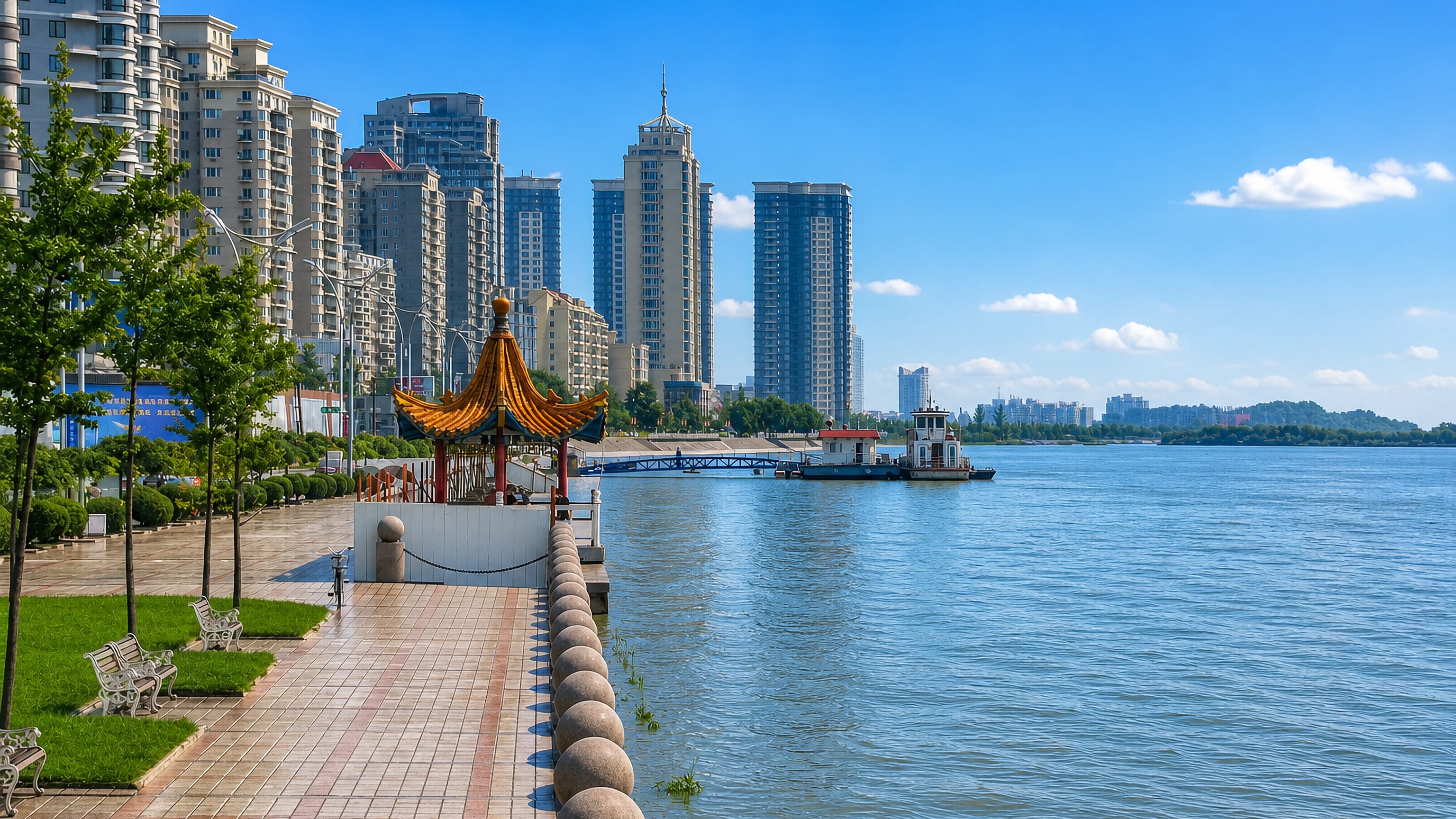 Riverside promenade with a gilded pavilion below high-rise towers along the Yalu in Yuanbao, Dandong.