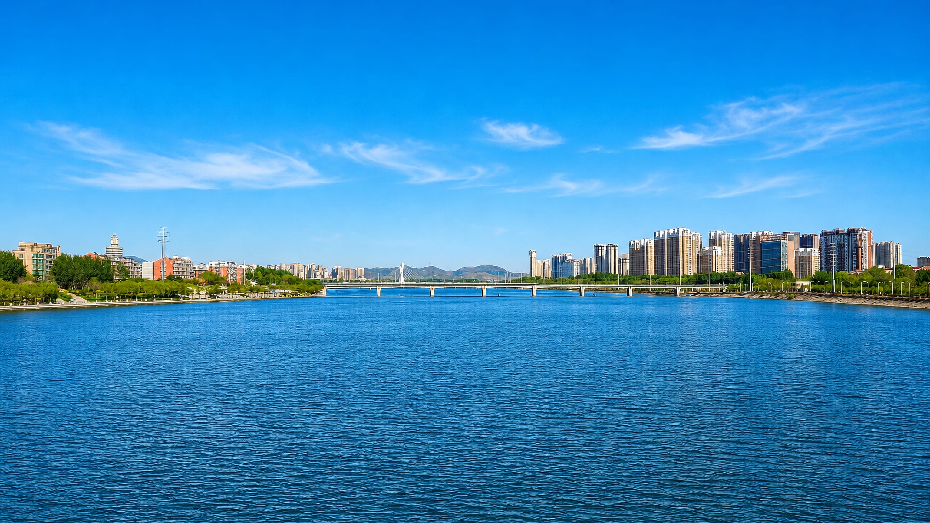 Wide river at Jinzhou, Liaoning, with a low bridge and riverfront apartment towers on the far bank.
