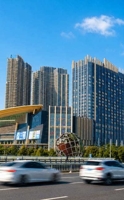 Shenyang's high-rise district with a globe sculpture and curved-roof arts hall beside a busy avenue.